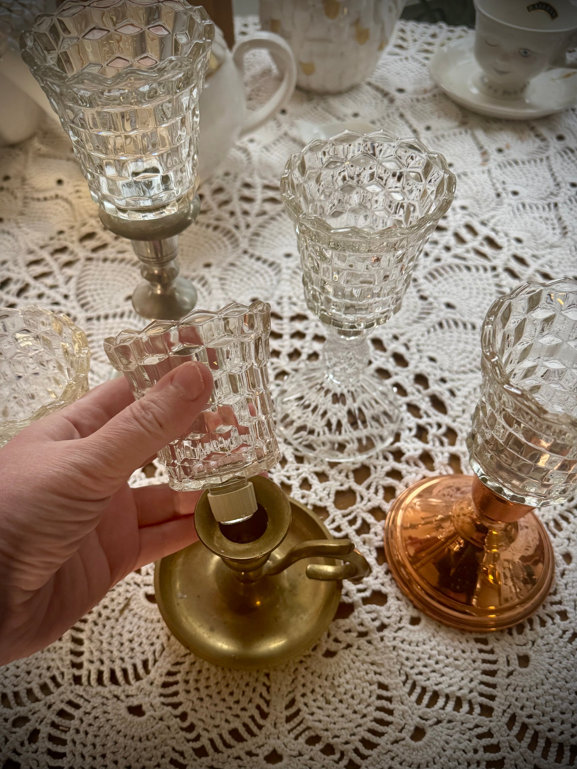 A collection of vintage glass votive holders with pegs and gaskets, displayed on a table with a lace tablecloth.