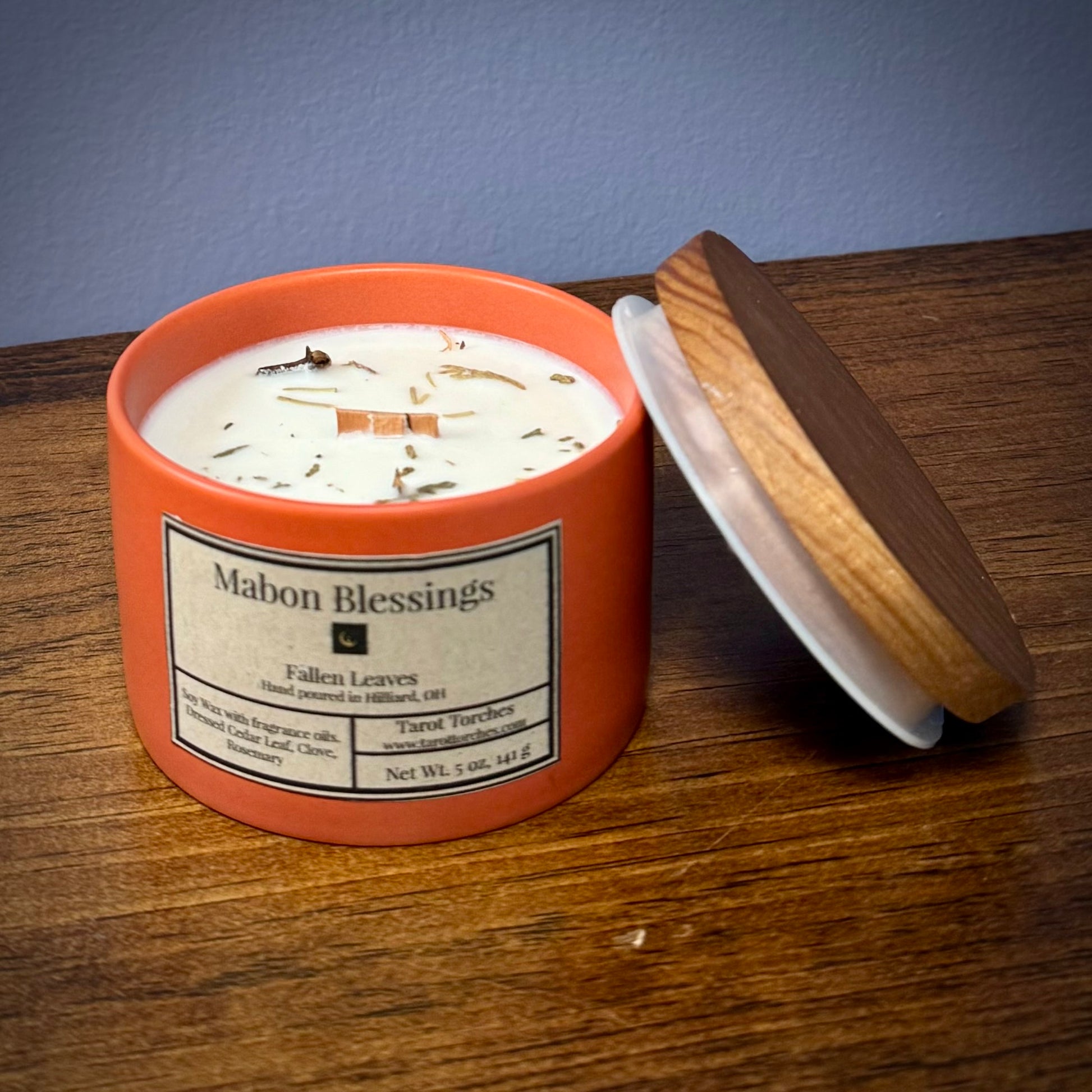 A burnt orange candle reading "Mabon Blessings" with an offset pine lid on a wooden surface.