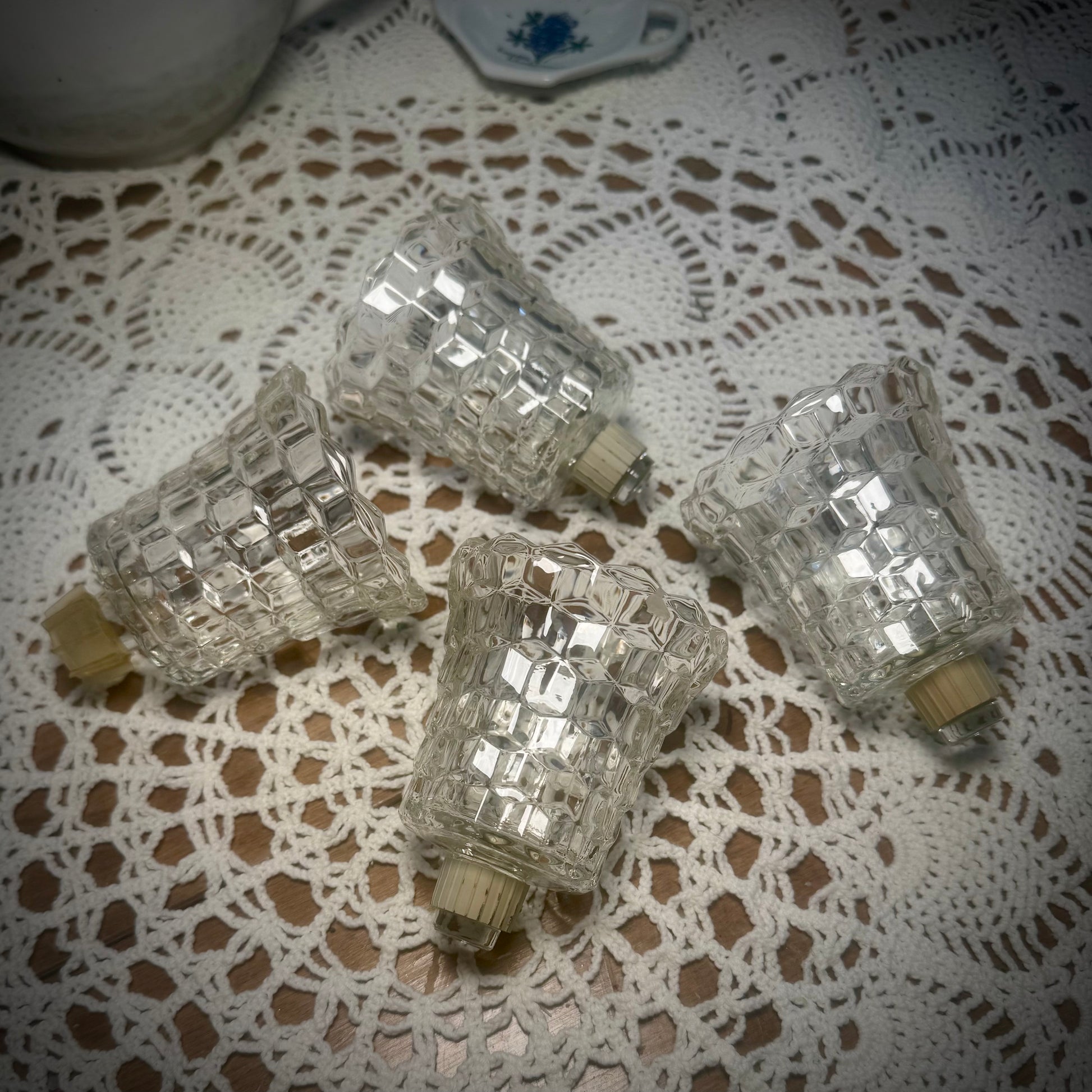 Four vintage glass votive candle holders with pegs and gaskets at the bottom, displayed on a table with a lace tablecloth