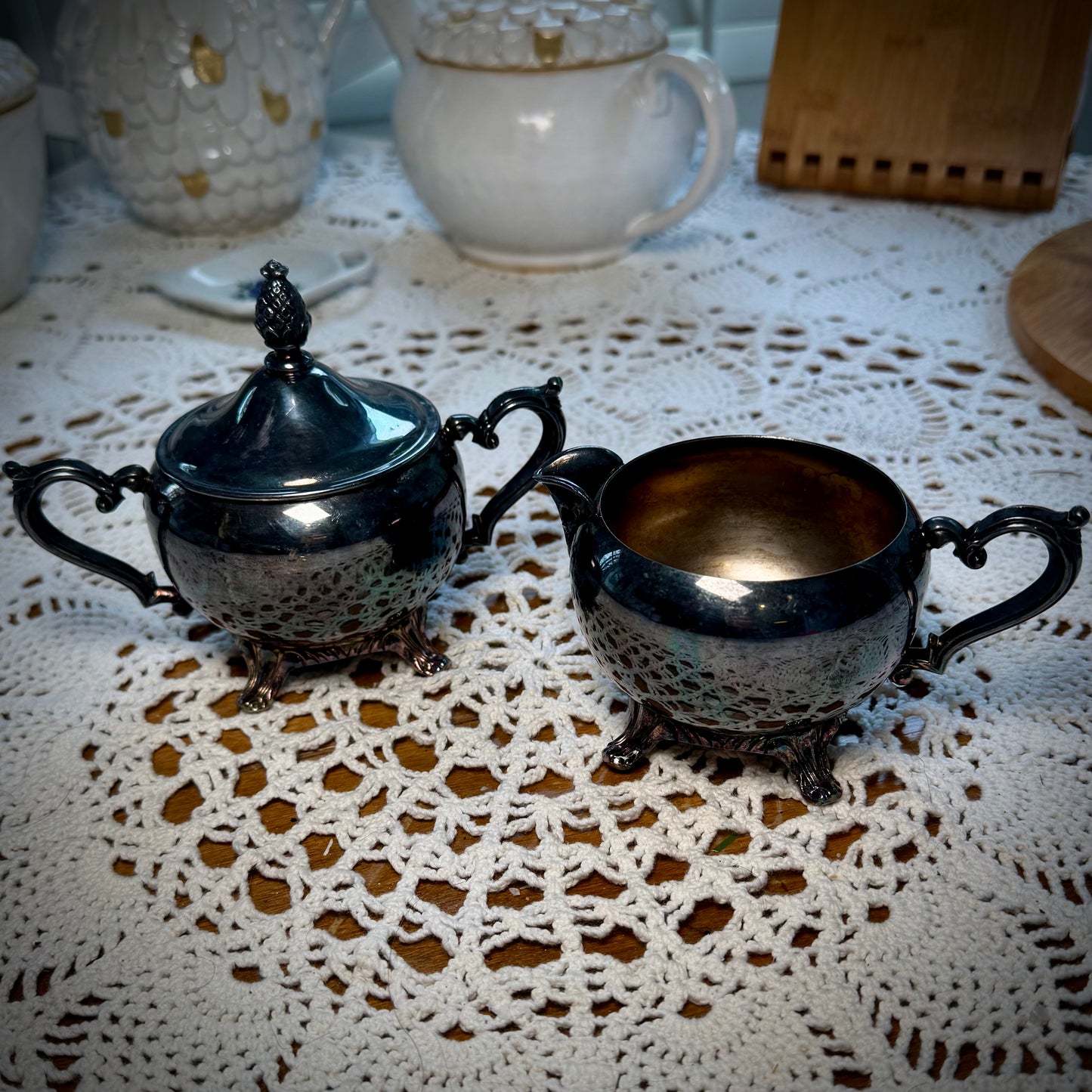 A vintage WM Rogers Silverplate cream and sugar set on a table with a lace tablecloth.