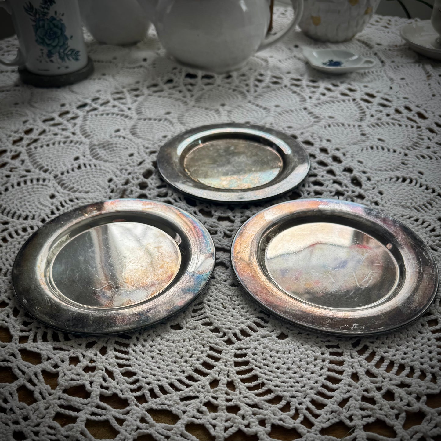 Three round silverplate Offering Plates on a lace surface, reflecting light and showing signs of wear.