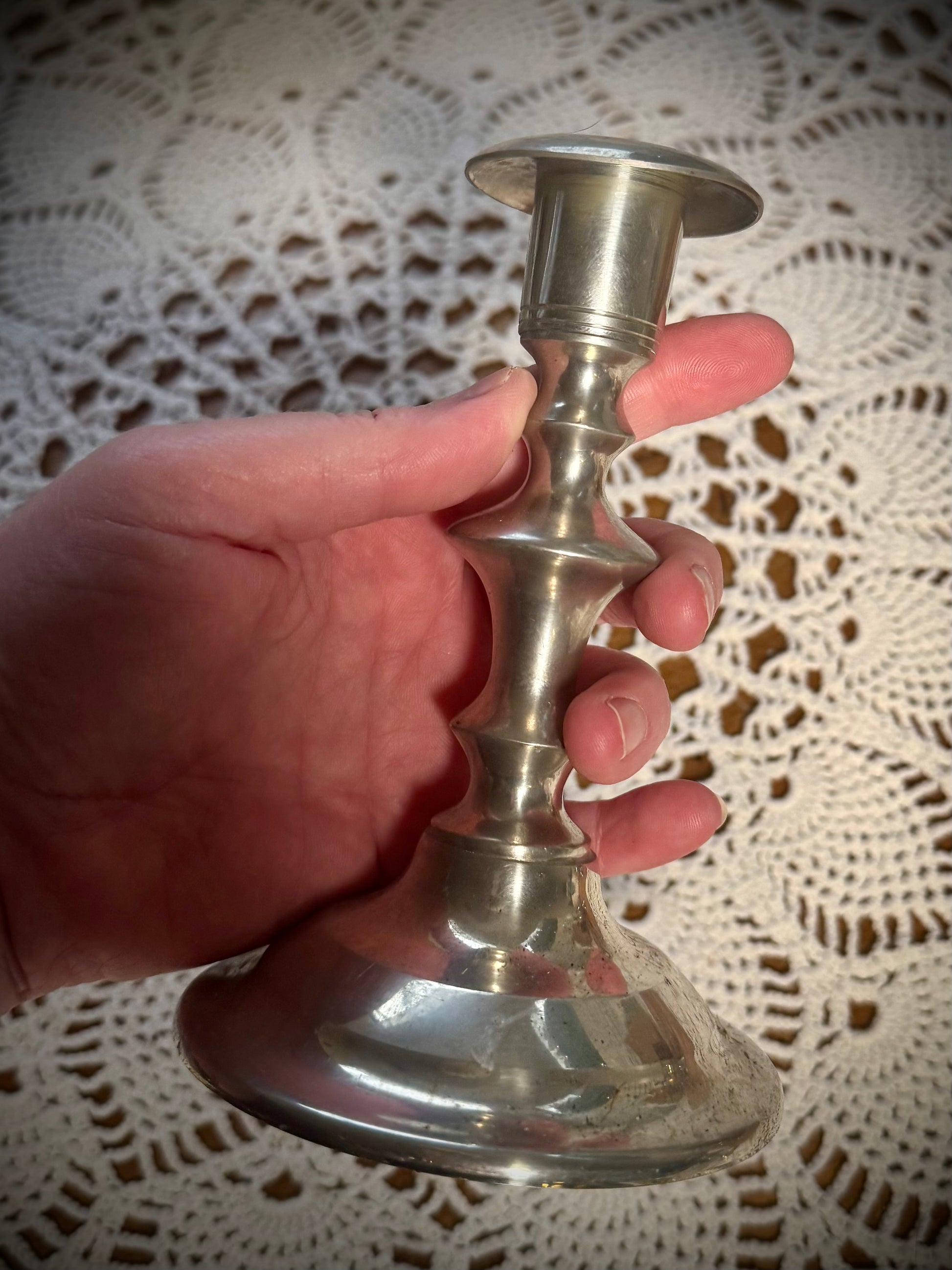 A hand sized vintage pewter candlestick being held above a table with a white lace tablecloth