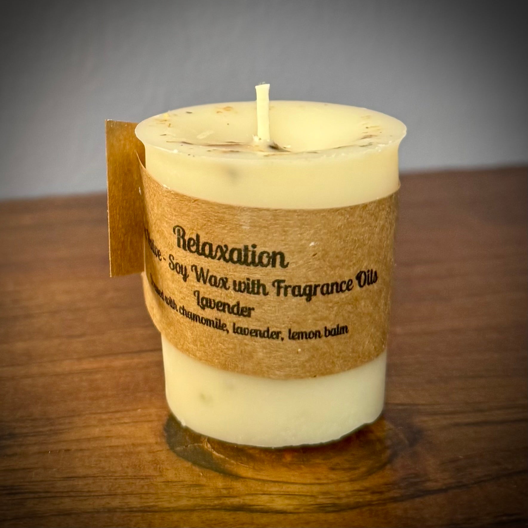 A soy wax votive candle with a cotton wick, labeled 'Relaxation' with natural herbs on a wooden surface.