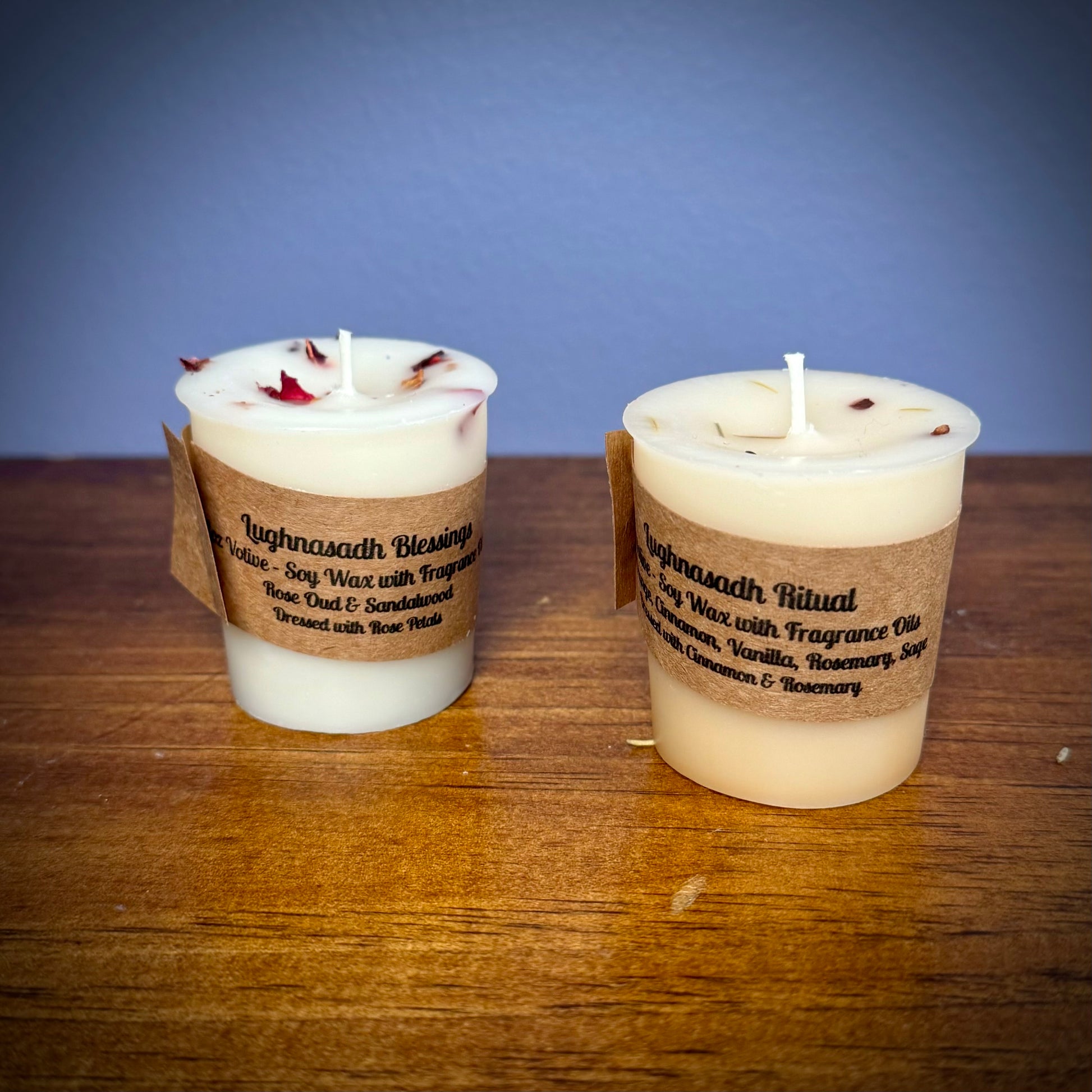 Two white votive candles with kraft labels sit on a wooden surface.