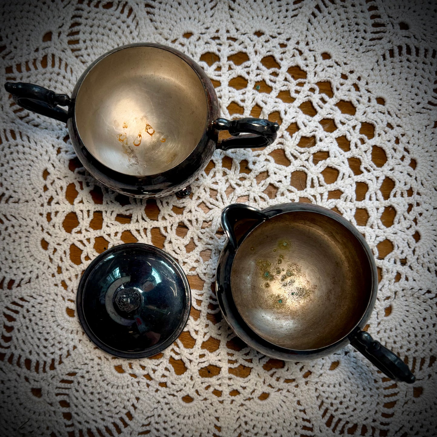 A vintage WM Rogers Silverplate cream and sugar set on a table with a lace tablecloth.