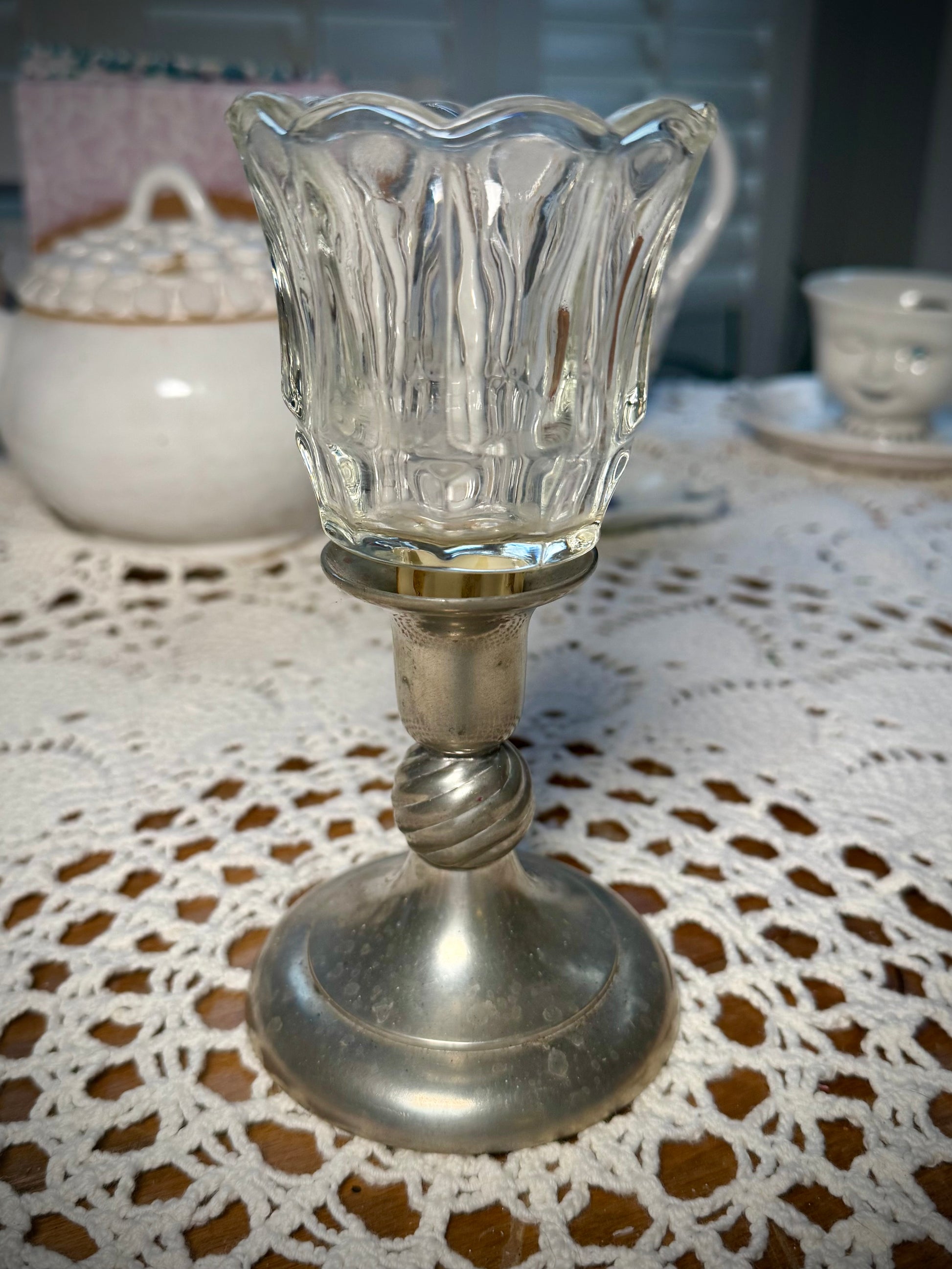 A clear glass votive candle holder with a textured design, placed in a pewter candlestick holder