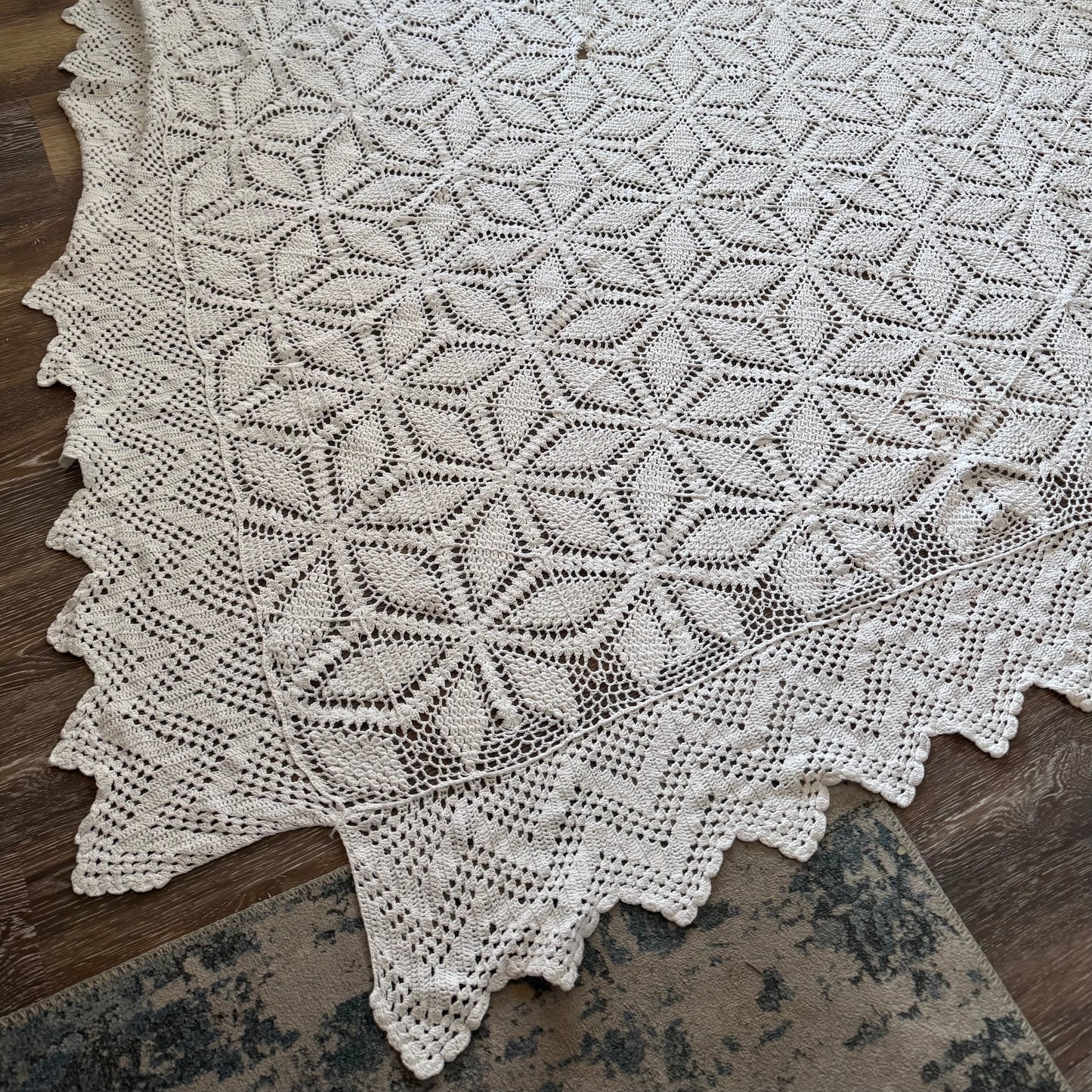 A vintage crochet blanket with a geometric pattern, predominantly in white, laid out on a wooden surface.