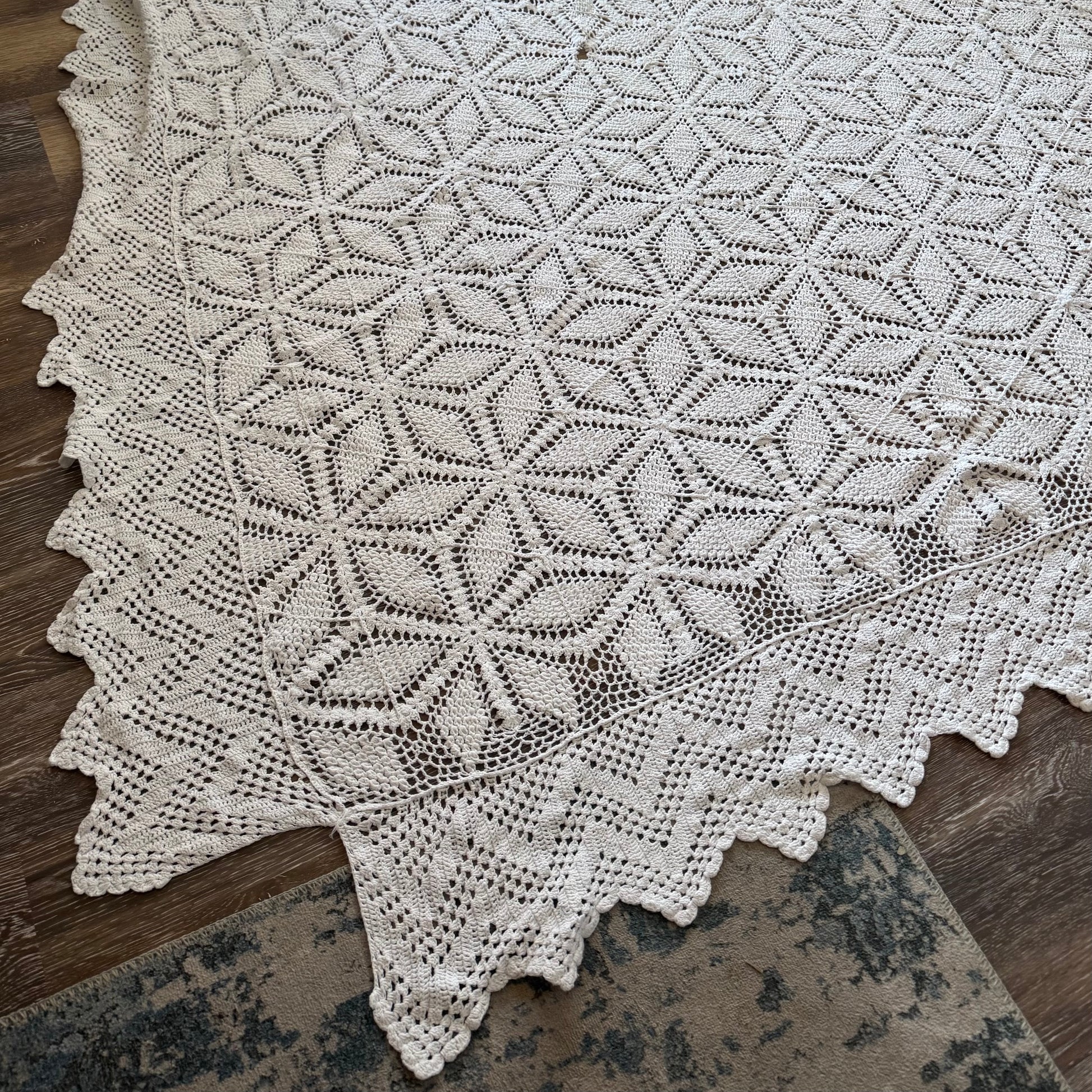A vintage crochet blanket with a geometric pattern, predominantly in white, laid out on a wooden surface.