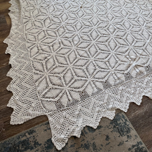 A vintage crochet blanket with a geometric pattern, predominantly in white, laid out on a wooden surface.