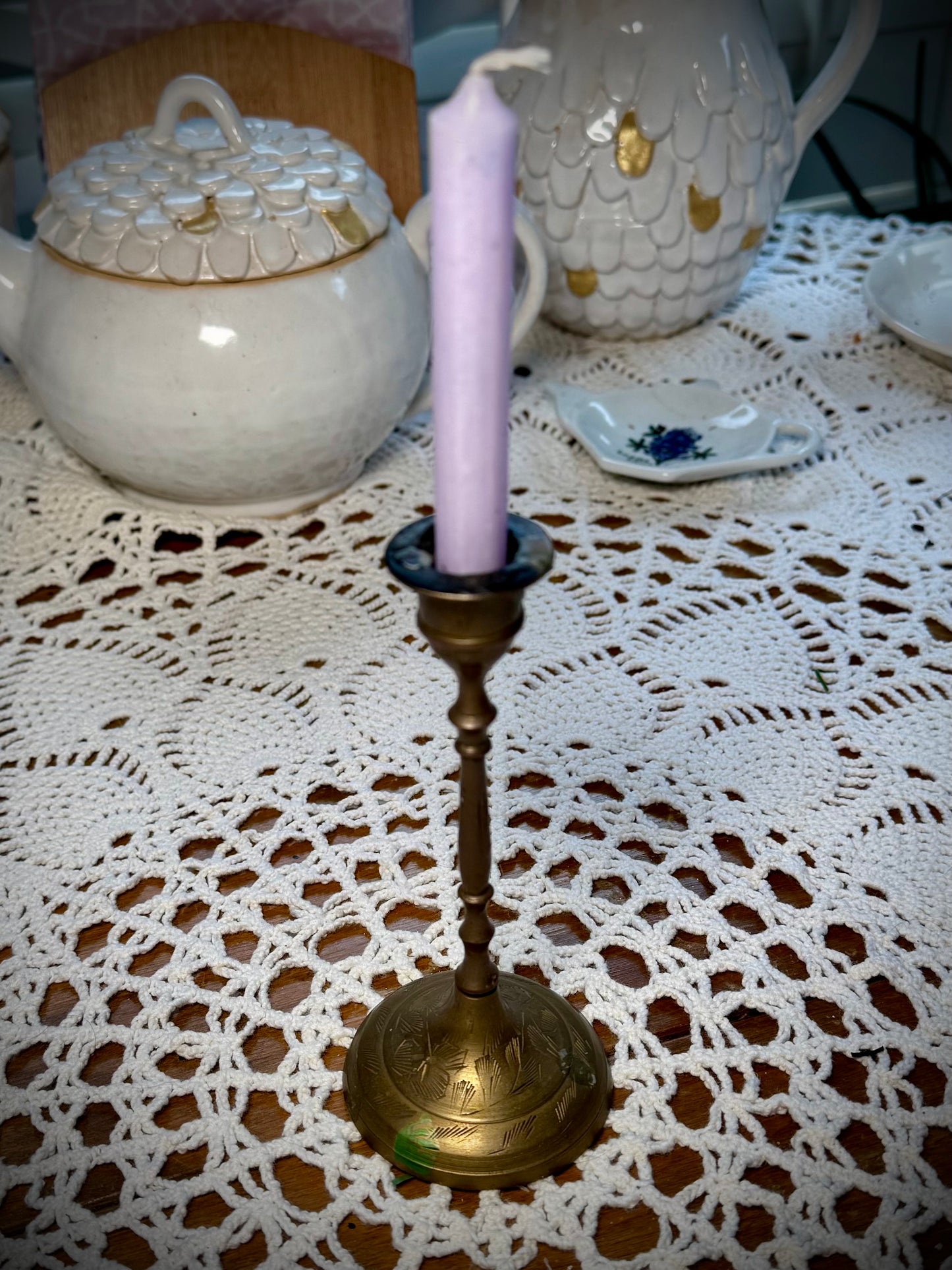 A vintage brass candle holder with etching on the base holding a light purple chime candle