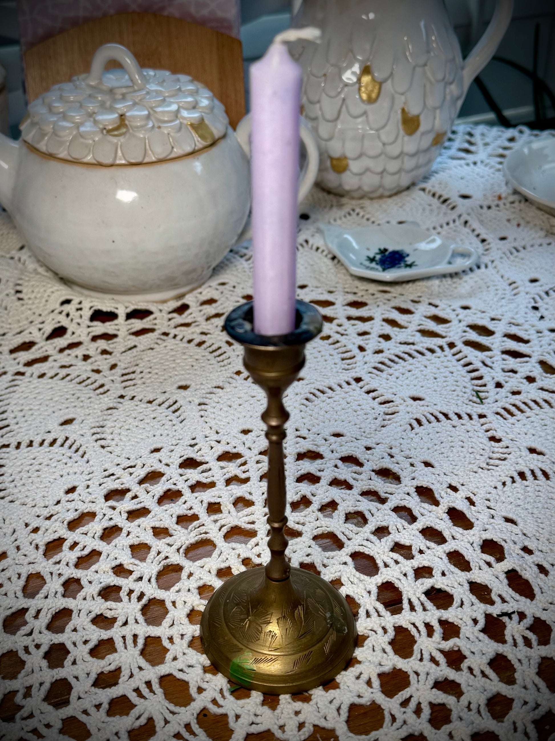 A vintage brass candle holder with etching on the base holding a light purple chime candle