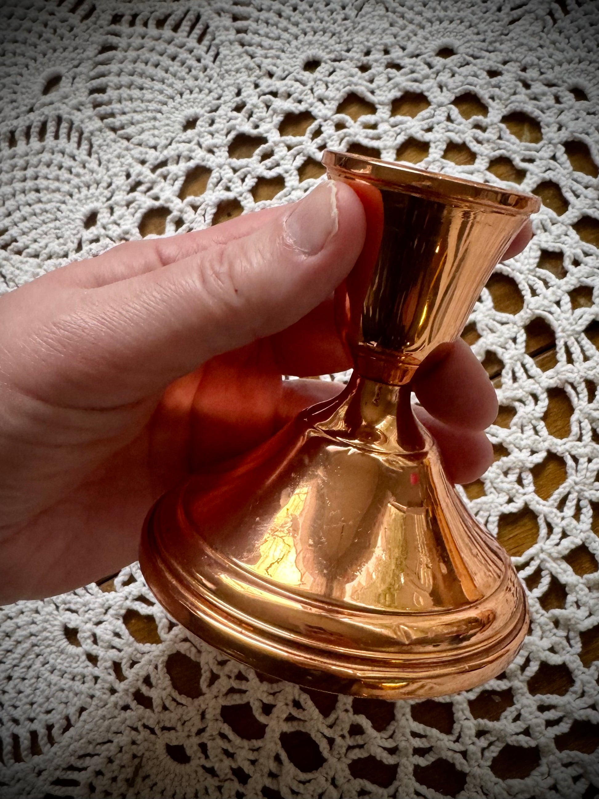 A single vintage copper candle holder being held over a white lace tablecloth.