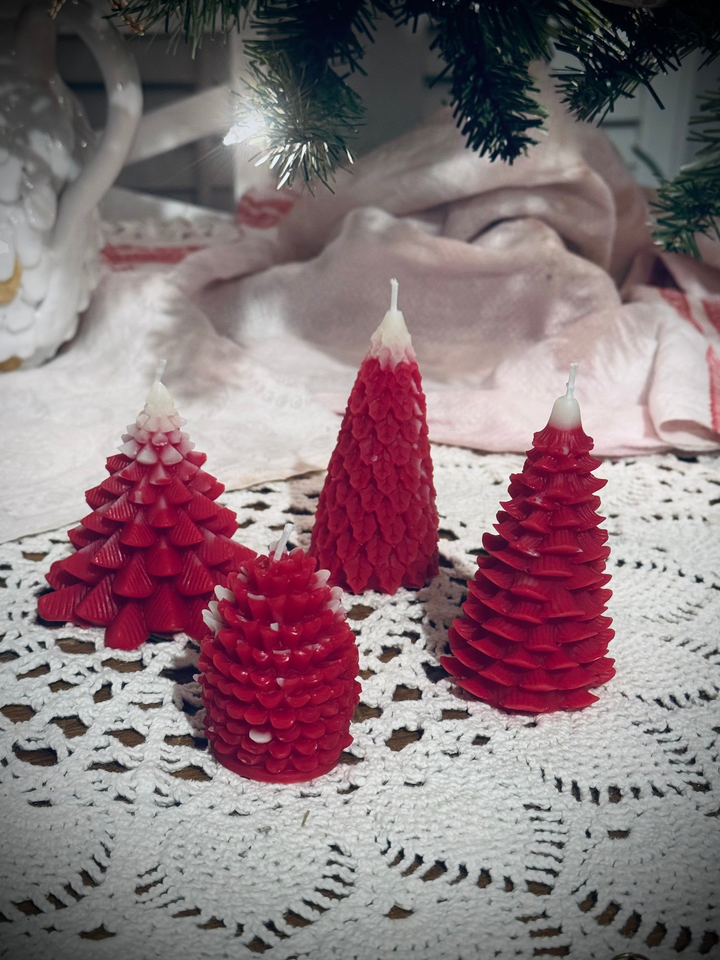 Four different molded red tree candles in front of a decorated Christmas tree.