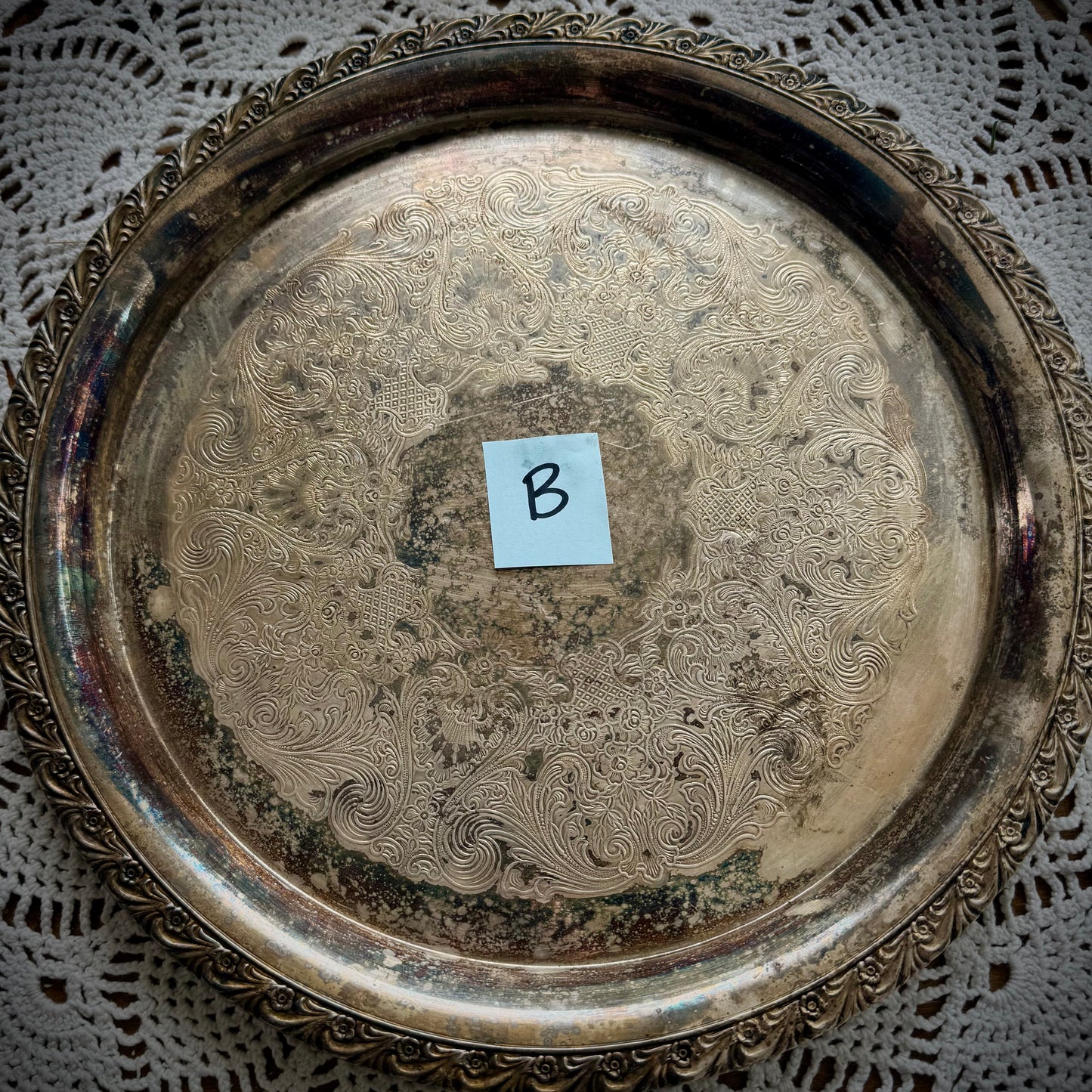 A silverplate round offering tray is displayed on a white lace surface. The tray has a post-in with the letter "B"