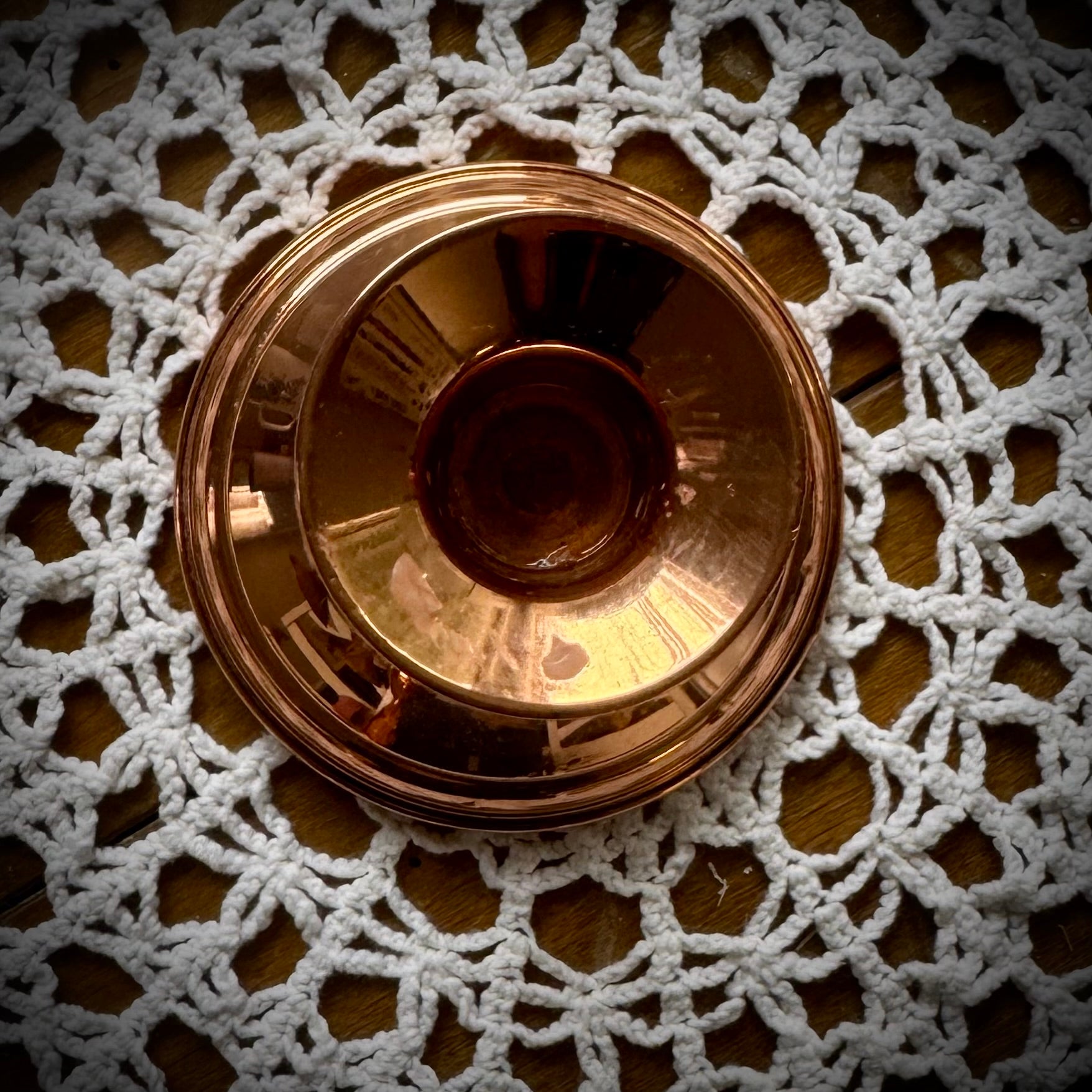 A single vintage copper candle holder displayed on a lace tablecloth.