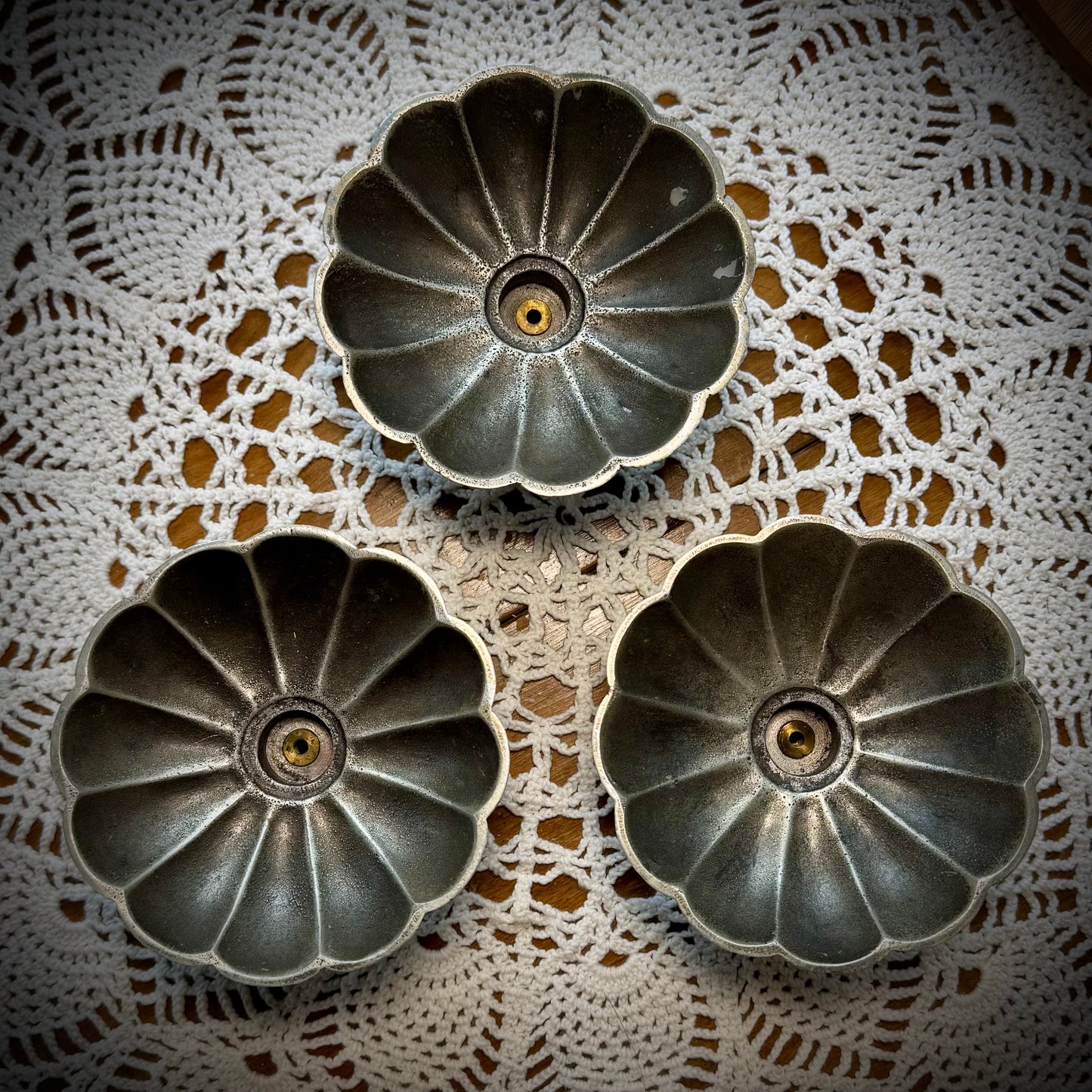 Aerial view of three vintage pewter swirled taper candle holders displayed on a table with a lace tablecloth.