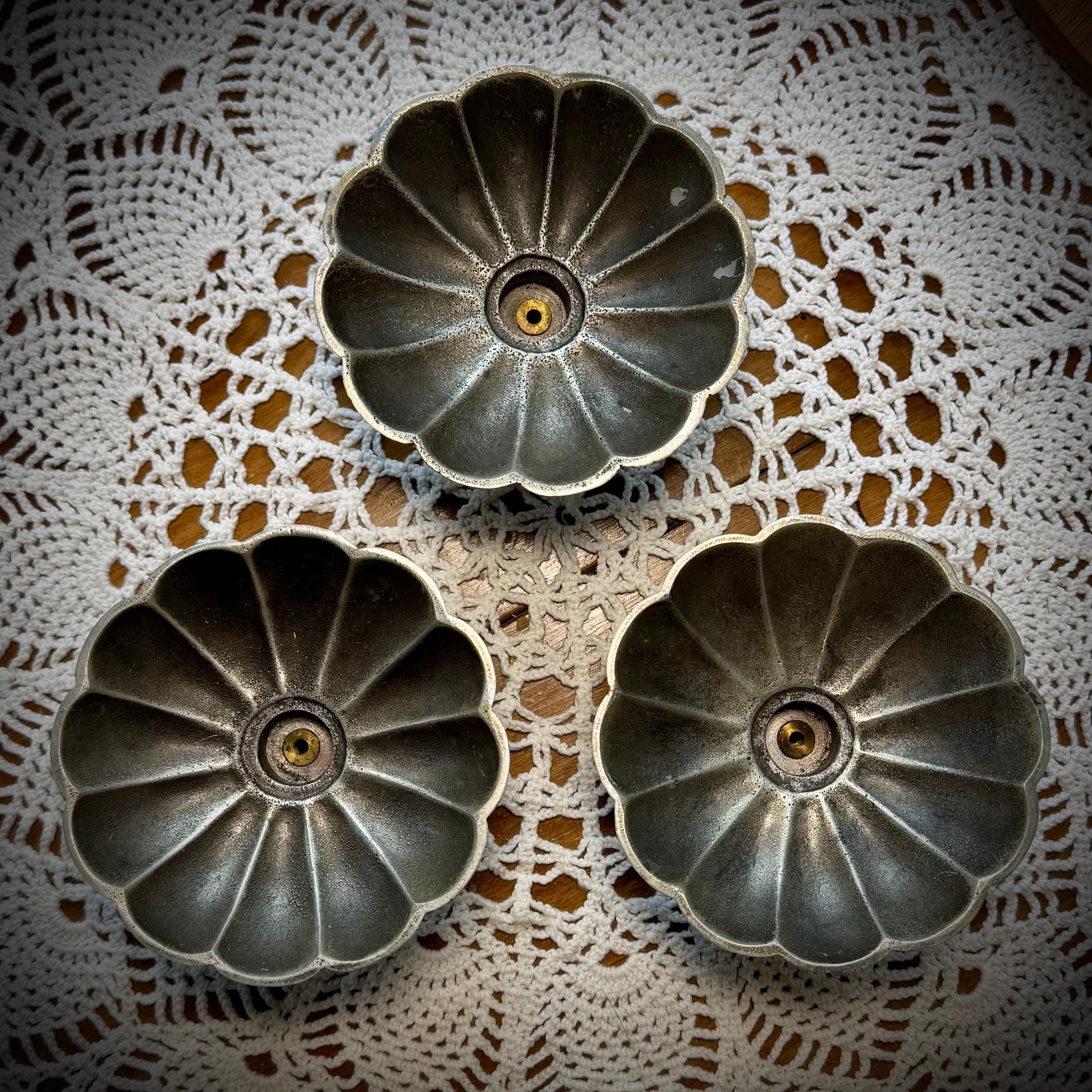 Aerial view of three vintage pewter swirled taper candle holders displayed on a table with a lace tablecloth.