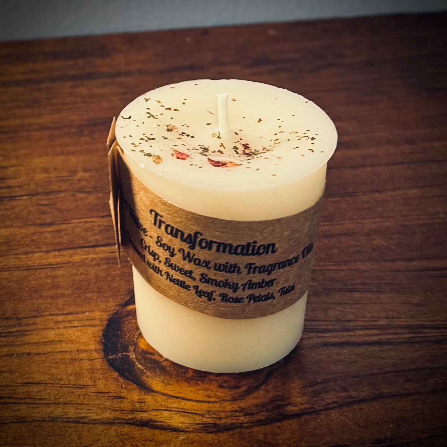A white votive with the label "transformation" sits on a wooden surface