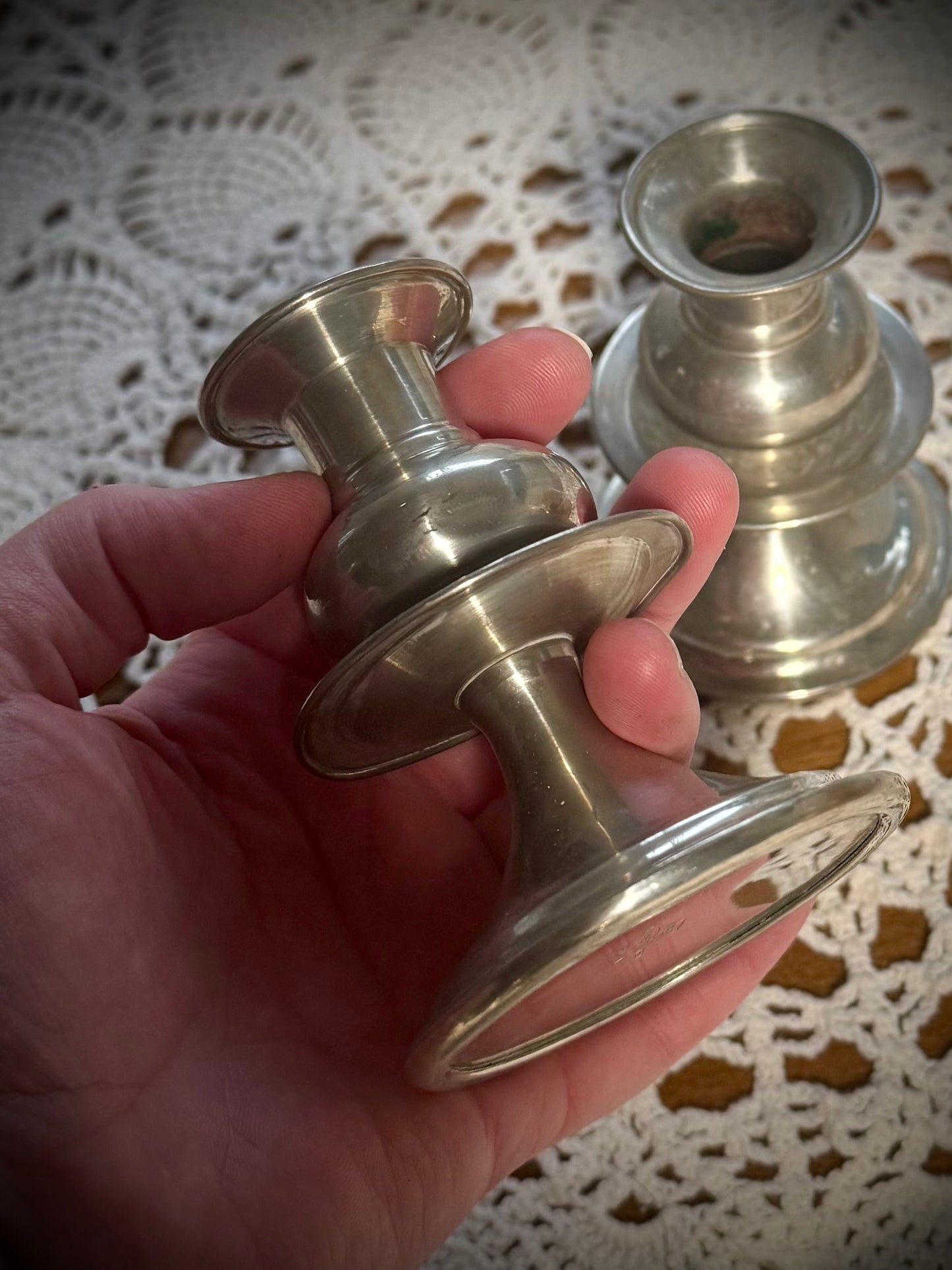 A small vintage pewter candlestick being held with an identical candlestick in the background