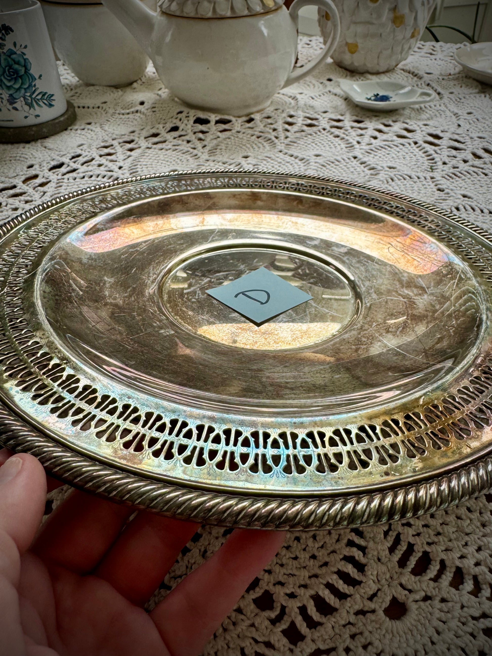 A silverplate round offering tray is displayed on a white lace surface. The tray has a post-it with the letter "D"