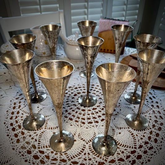 A set of vintage silver plate champagne flutes displayed on a table with a lace tablecloth.