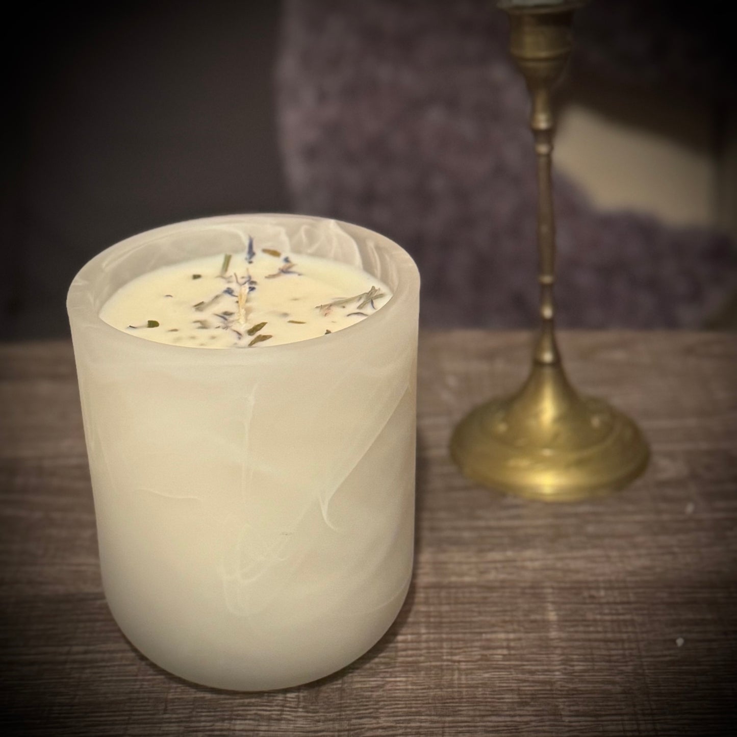 A white swirl glass candle sits on a table in front of a brass candlestick