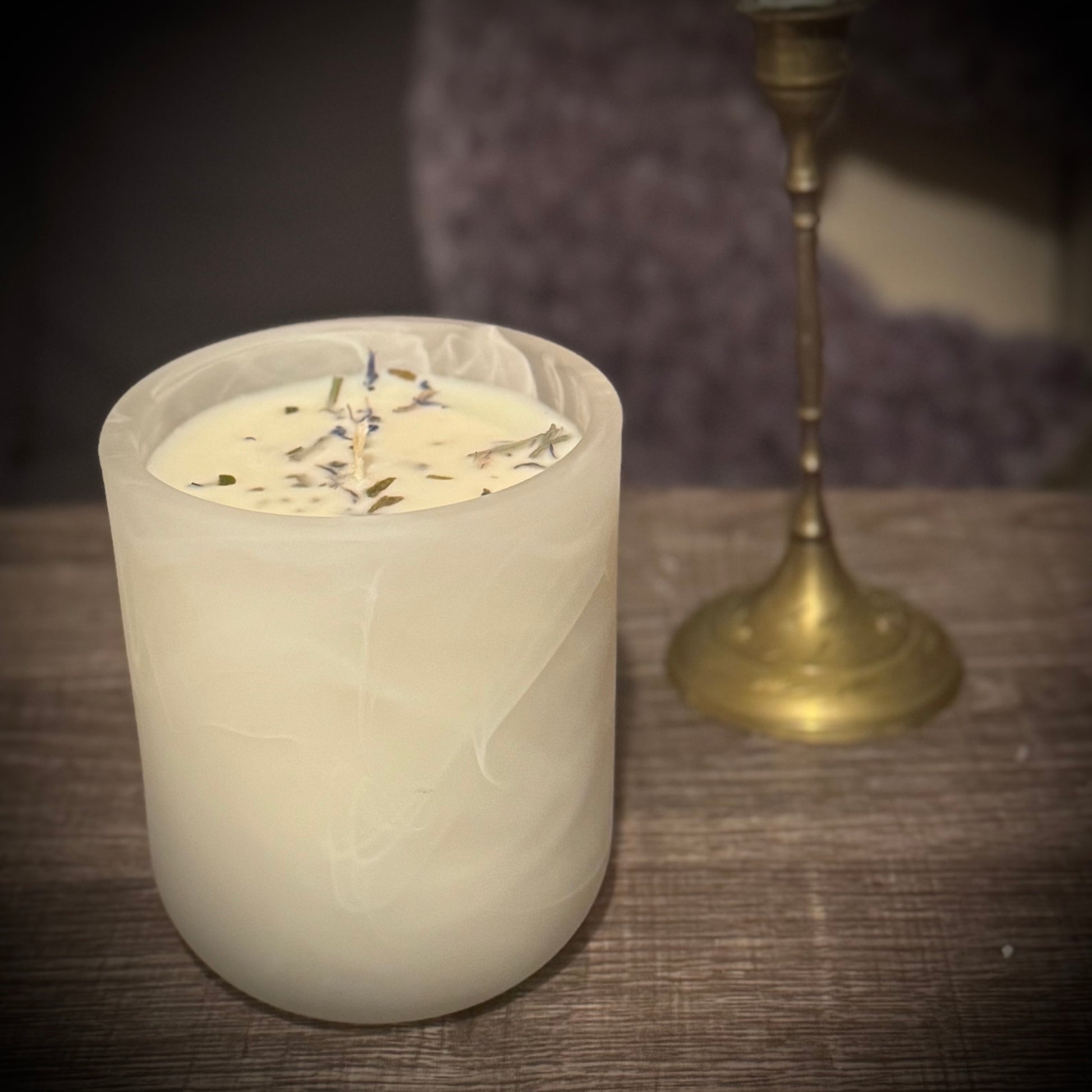 A white swirl glass candle sits on a table in front of a brass candlestick