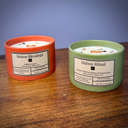 Two ceramic candles with pine lids, one labeled 'MABON BLESSINGS' and the other 'MABON RITUAL', on a wooden surface.