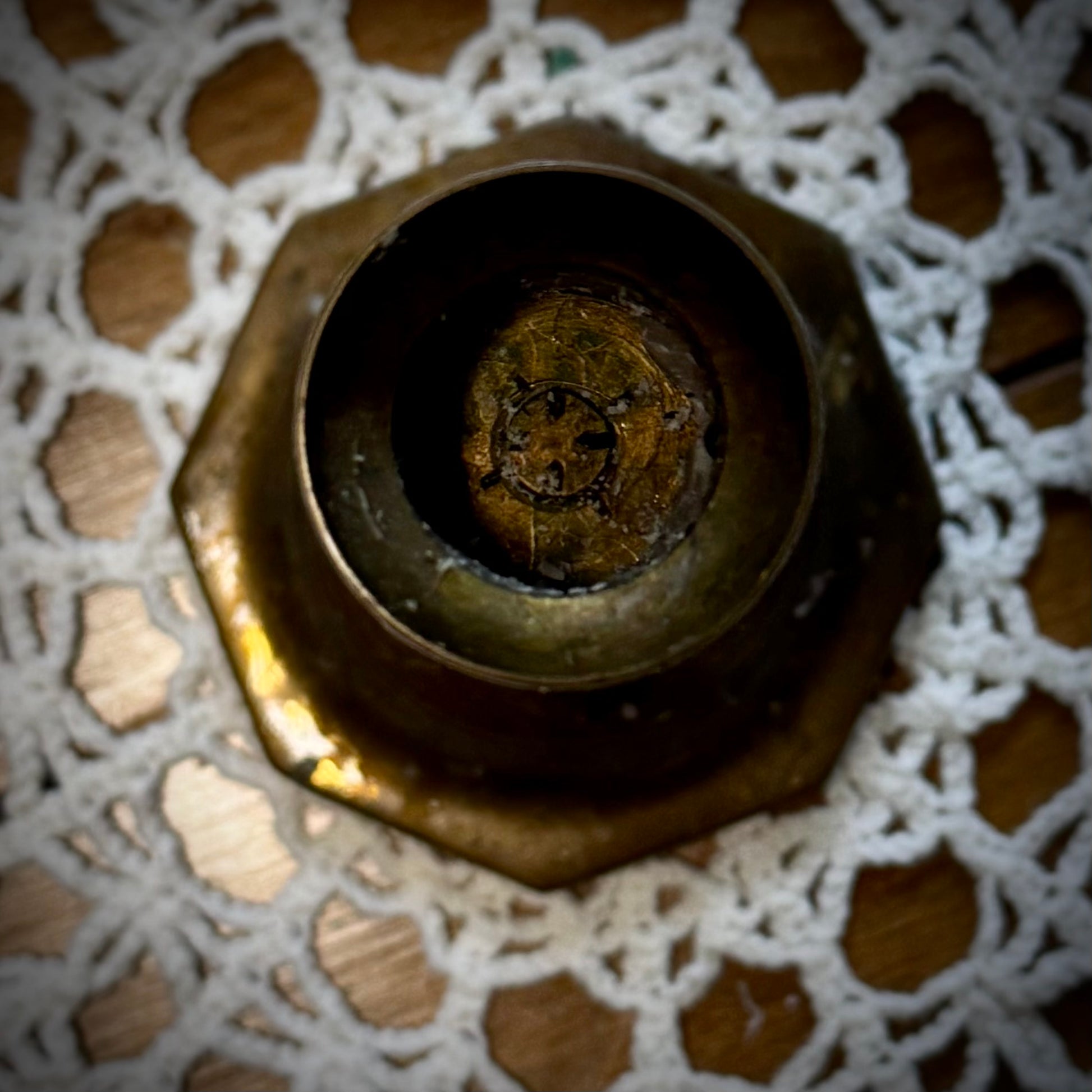 A vintage brass candle holder with an octagonal base, placed on a lace tablecloth.