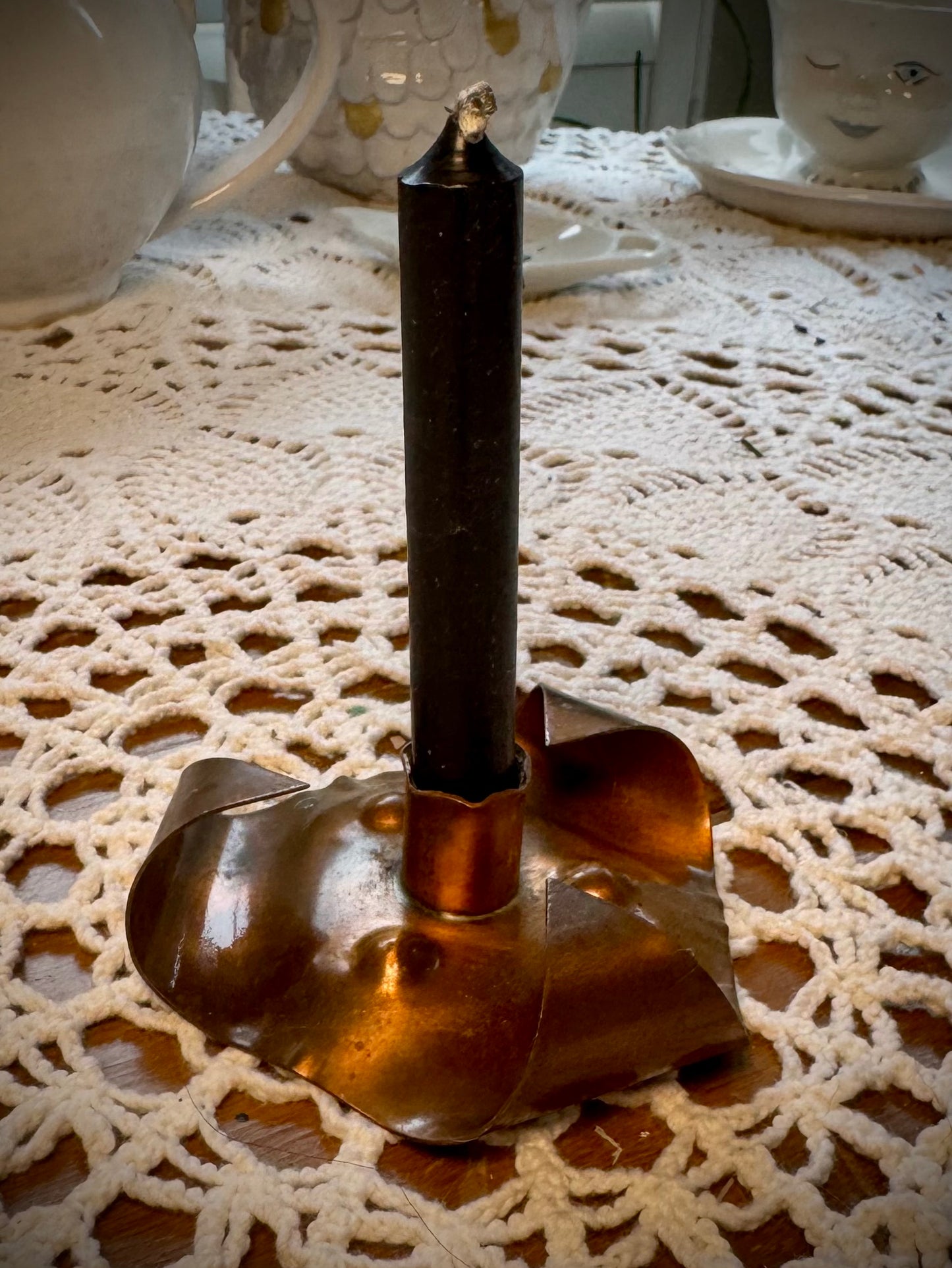 A vintage copper chime candle holder with a black chime candleon a table with a lace tablecloth.