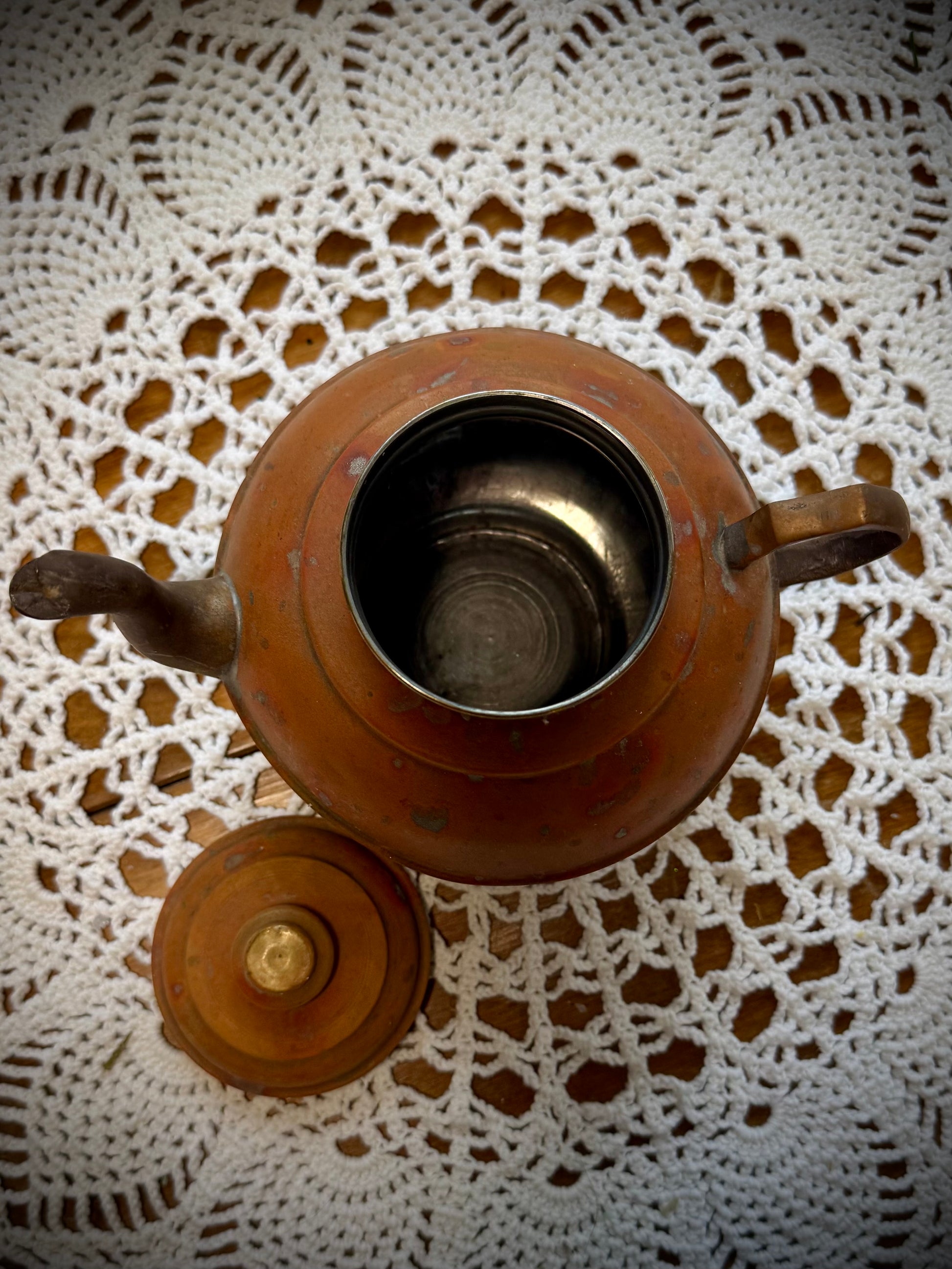 A vintage copper teapot with a Middle Eastern style design, placed on a table with the lid removed