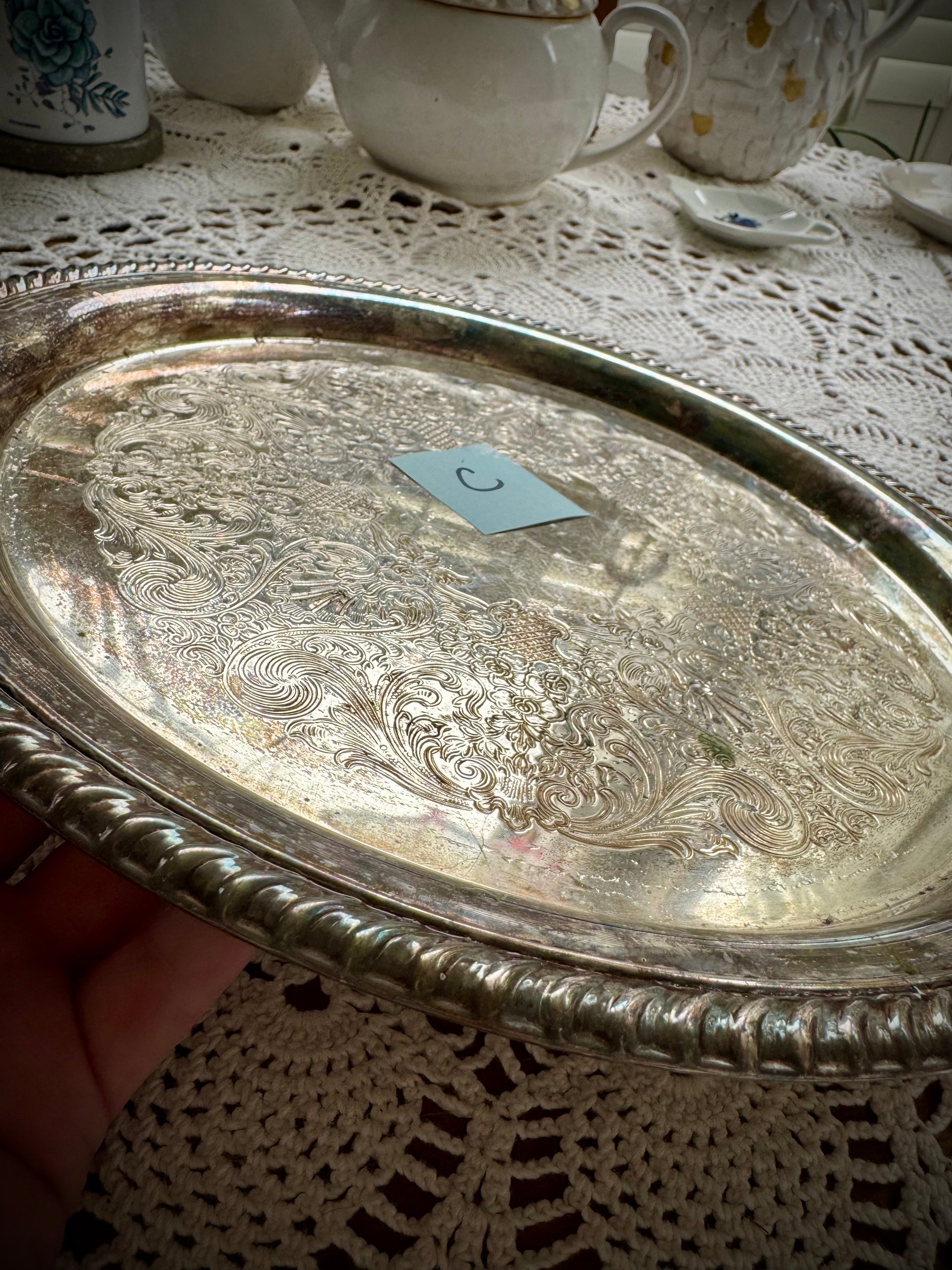 A silverplate round offering tray is displayed on a white lace surface. The tray has a post-it with the letter "C"