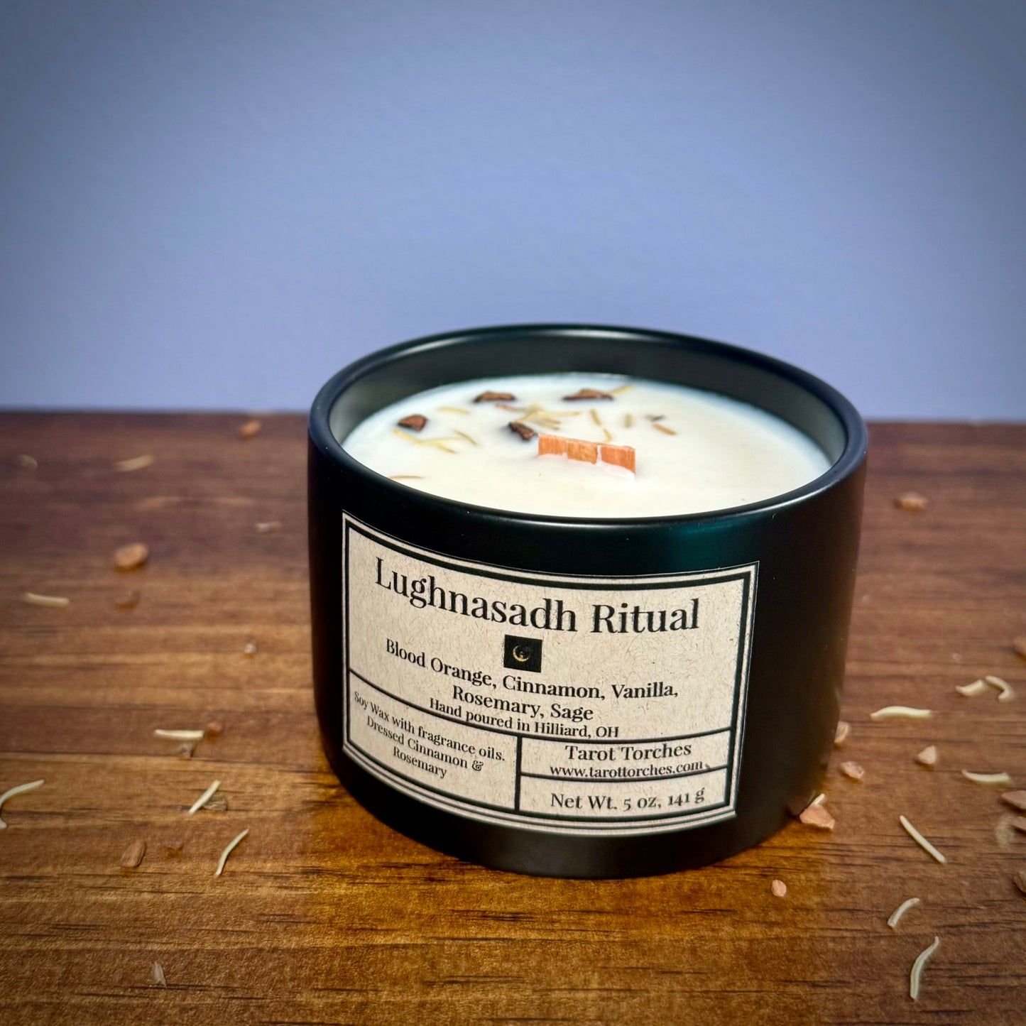 A ceramic candle labeled 'Lughnasadh Ritual' placed on a wooden surface against a purple background.