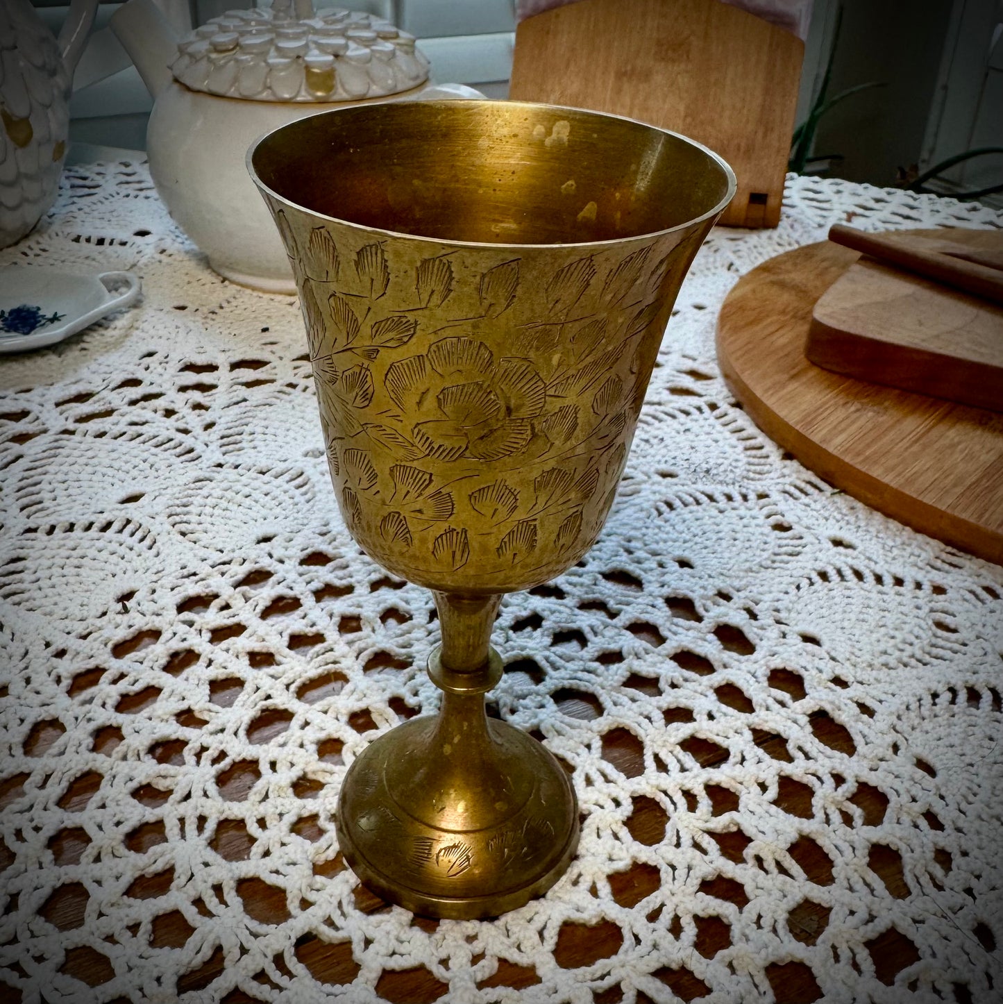 Etched brass colored goblet placed on a table with a white lace tablecloth
