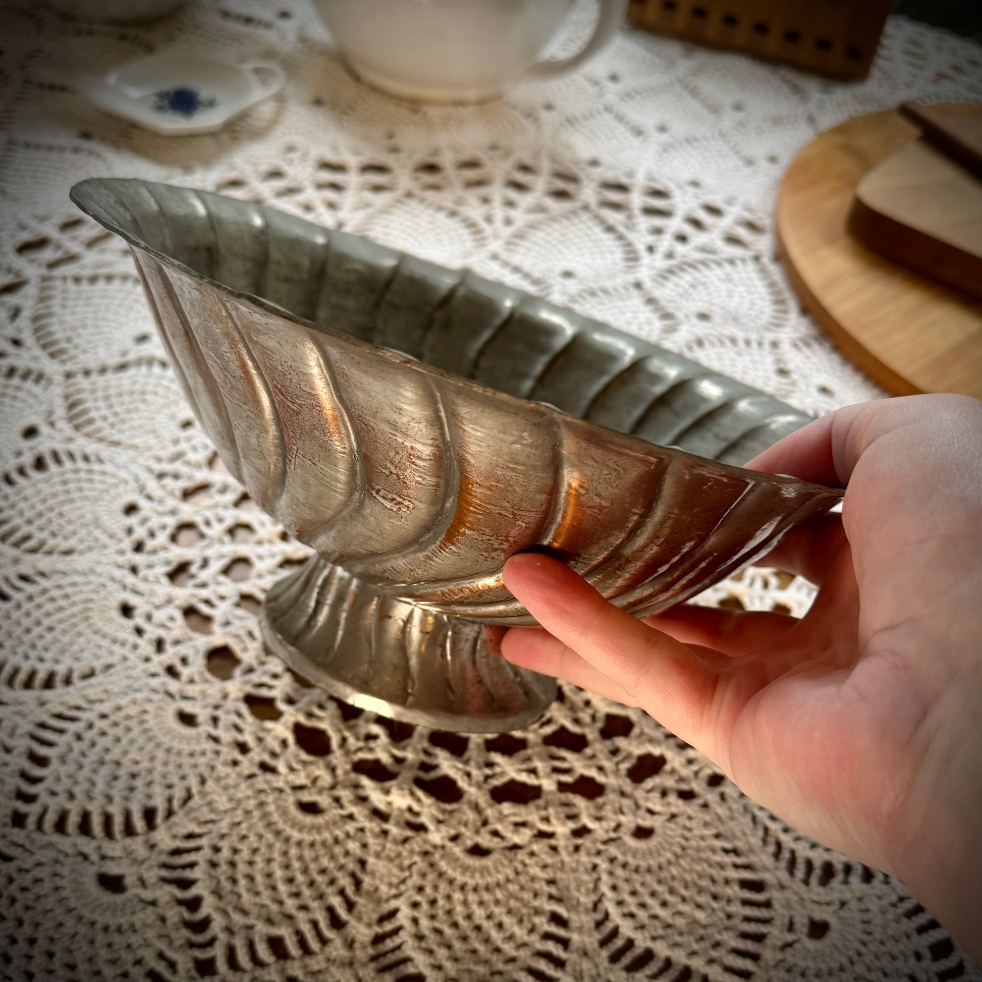 An antique swirl tinned copper pitcher being held to show the side view.
