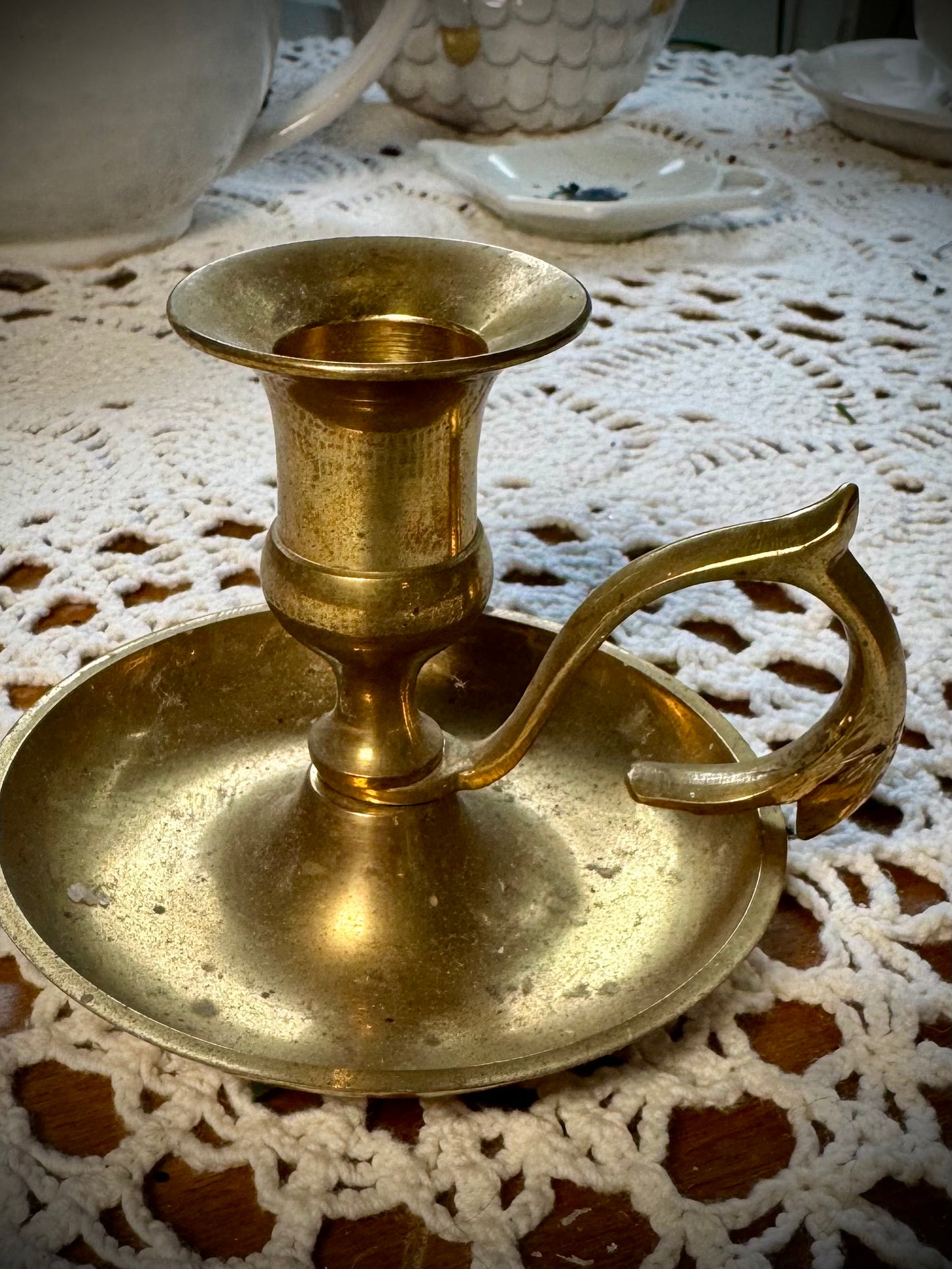A vintage brass candlestick with a finger loop on a table with a lace tablecloth.