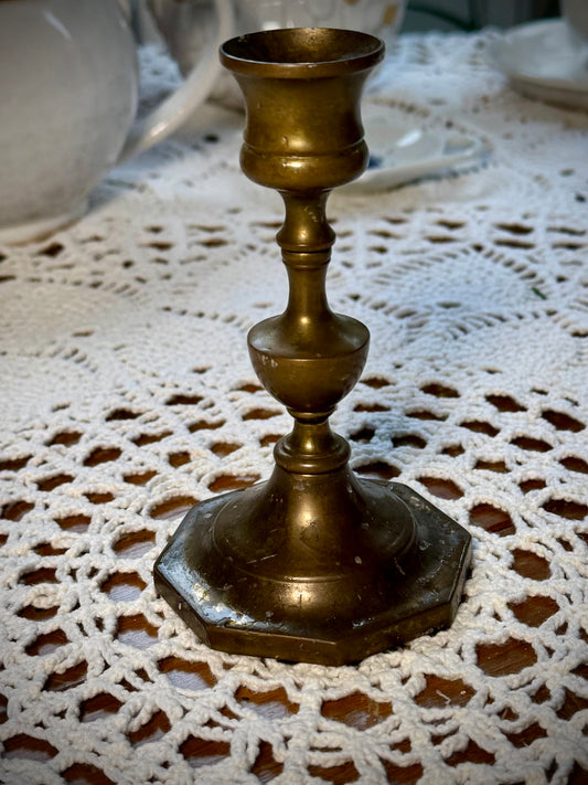 A vintage brass candle holder with an octagonal base, placed on a lace tablecloth.