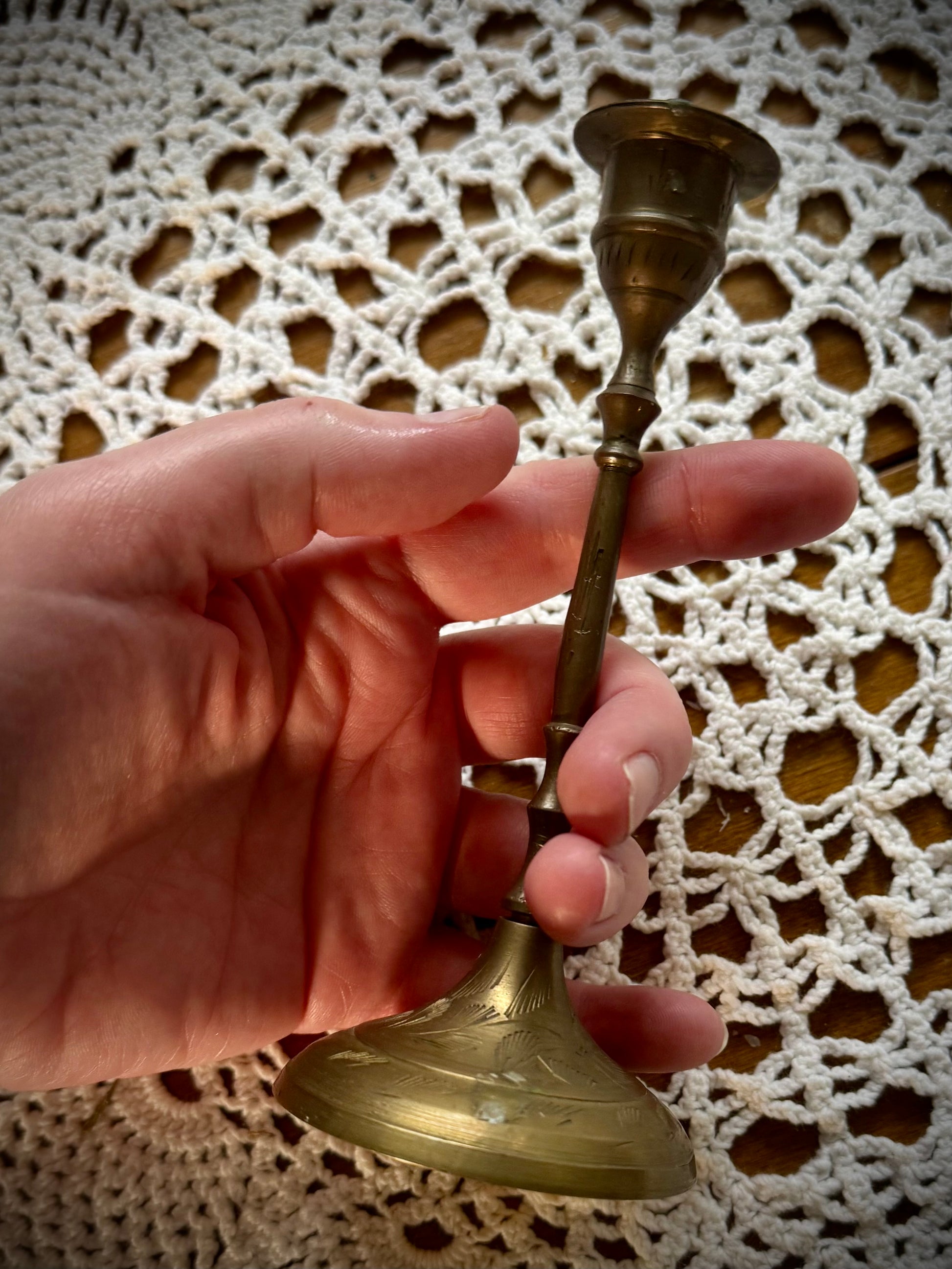 A vintage brass candle holder with etching on the base, displayed on a white lace tablecloth.