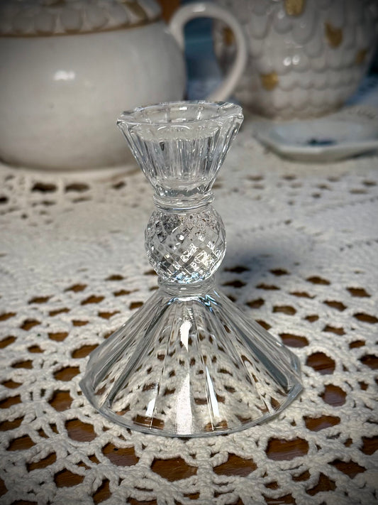 A small vintage clear glass candlestick on a table with a lace tablecloth, designed to hold a taper candle.