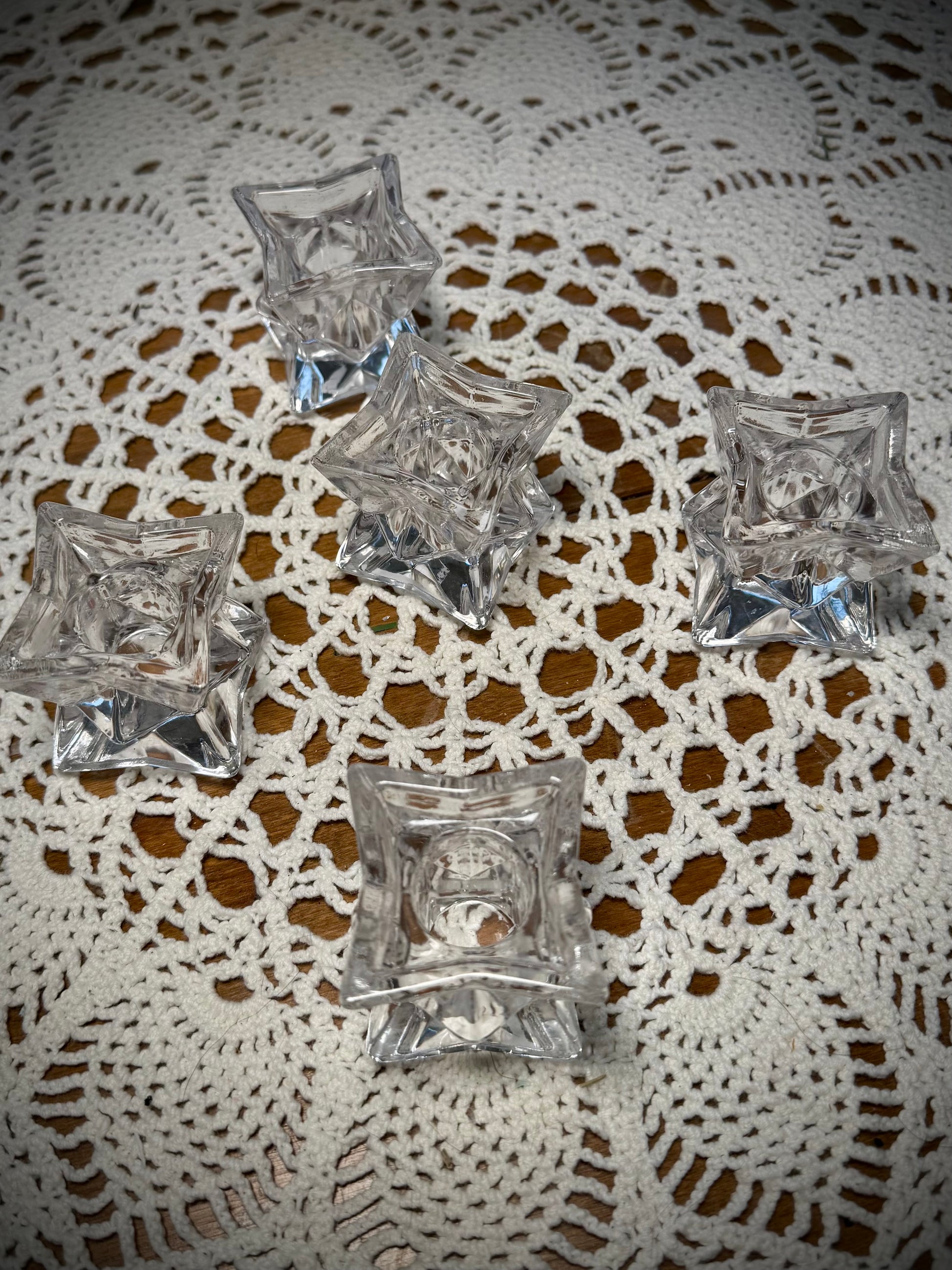 5 small glass geometric candle holders on a table with the white lace tablecloth.