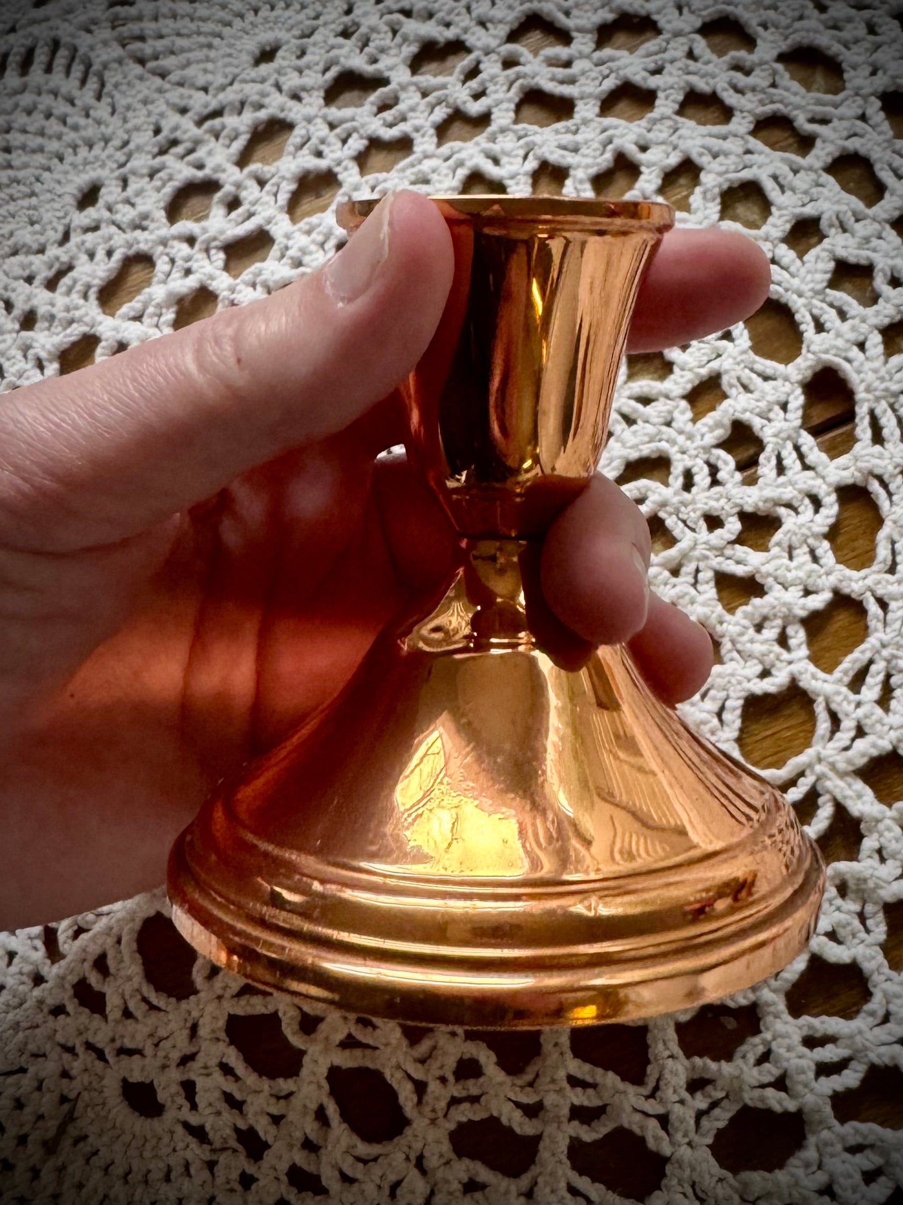 A single vintage copper candle holder being held over a white lace tablecloth.