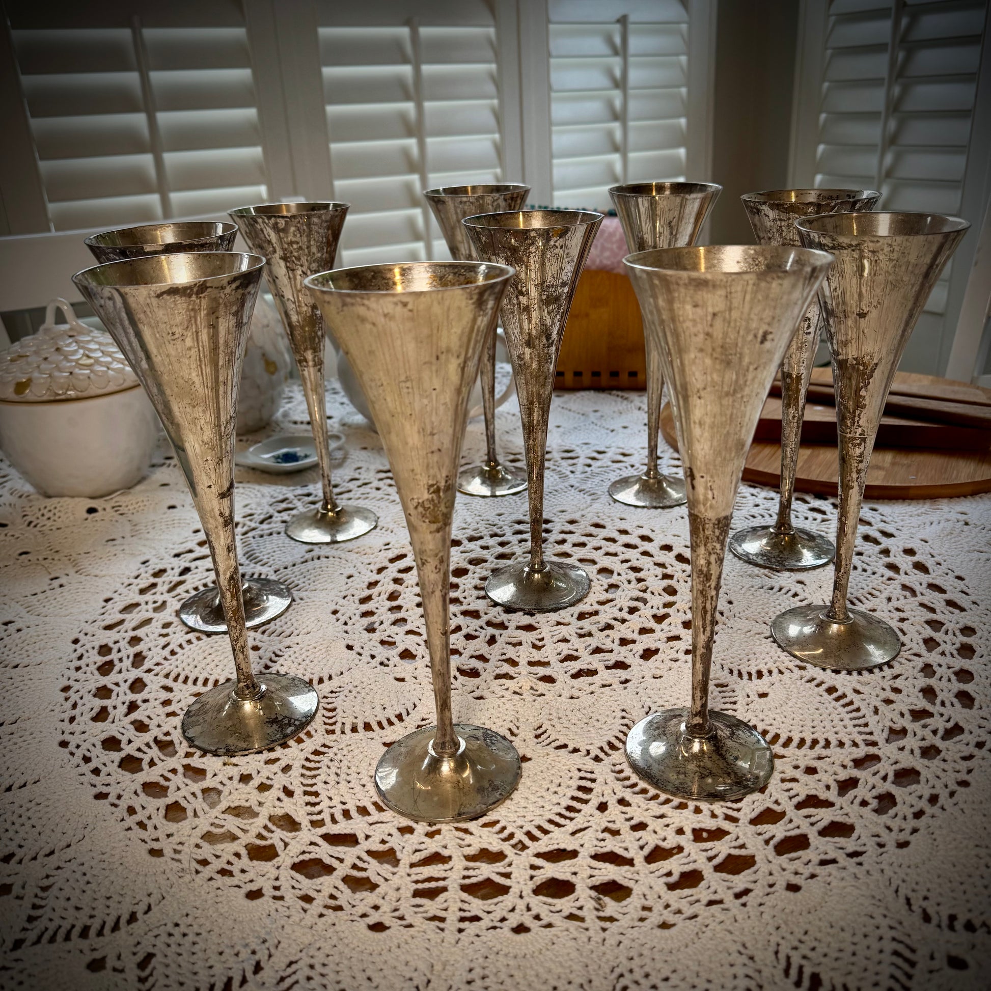 A set of vintage silver plate champagne flutes displayed on a table with a lace tablecloth.
