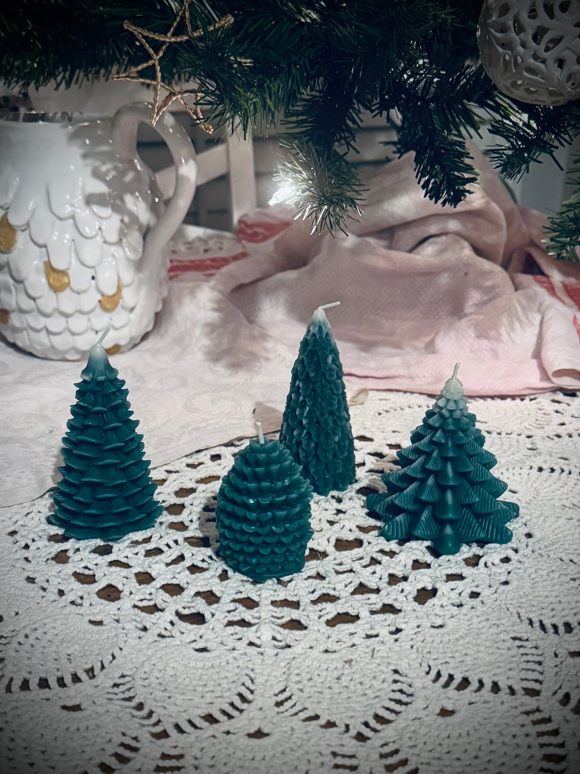 Four different molded green tree candles in front of a decorated Christmas tree.