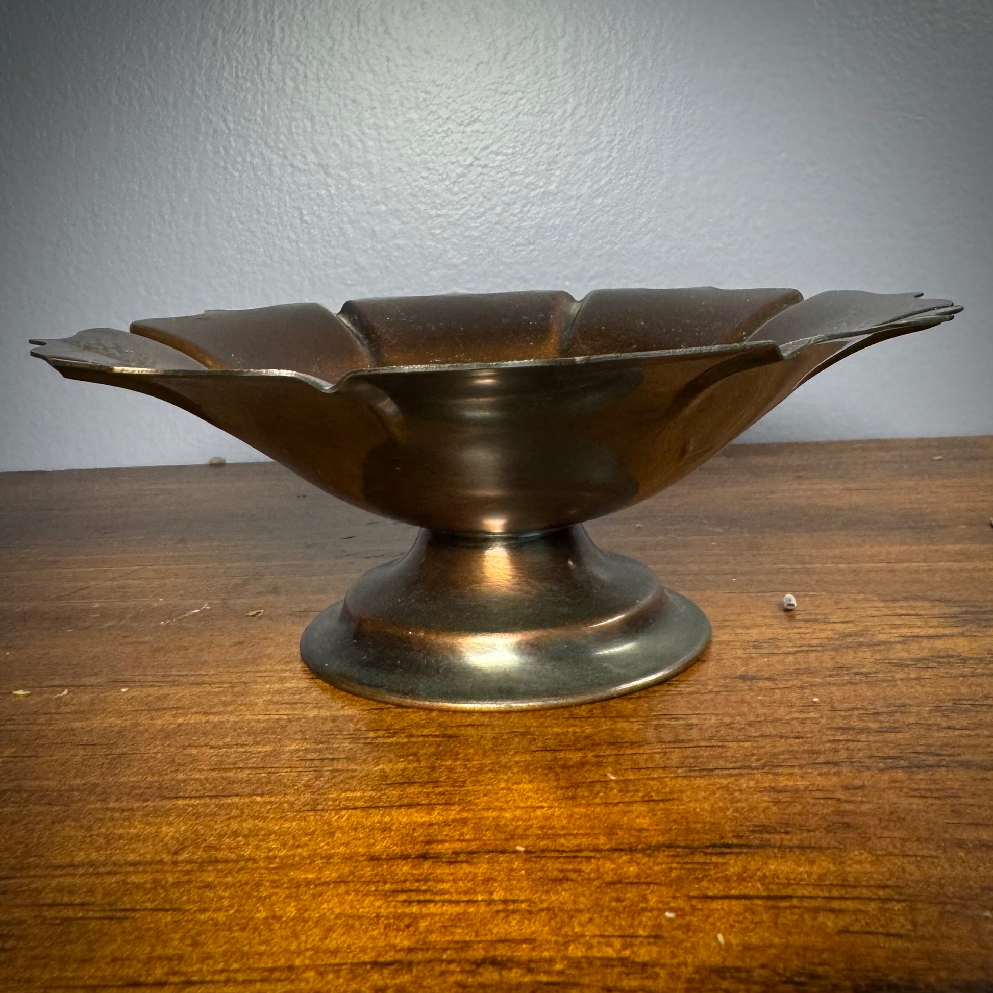 A vintage ritual bowl with a scalloped edge and a deep dark copper color, placed on a short and sturdy stand.