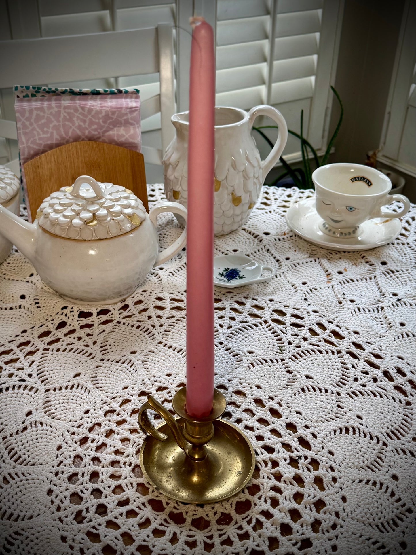 A vintage brass candlestick with a finger loop holding a tall pink taper candle