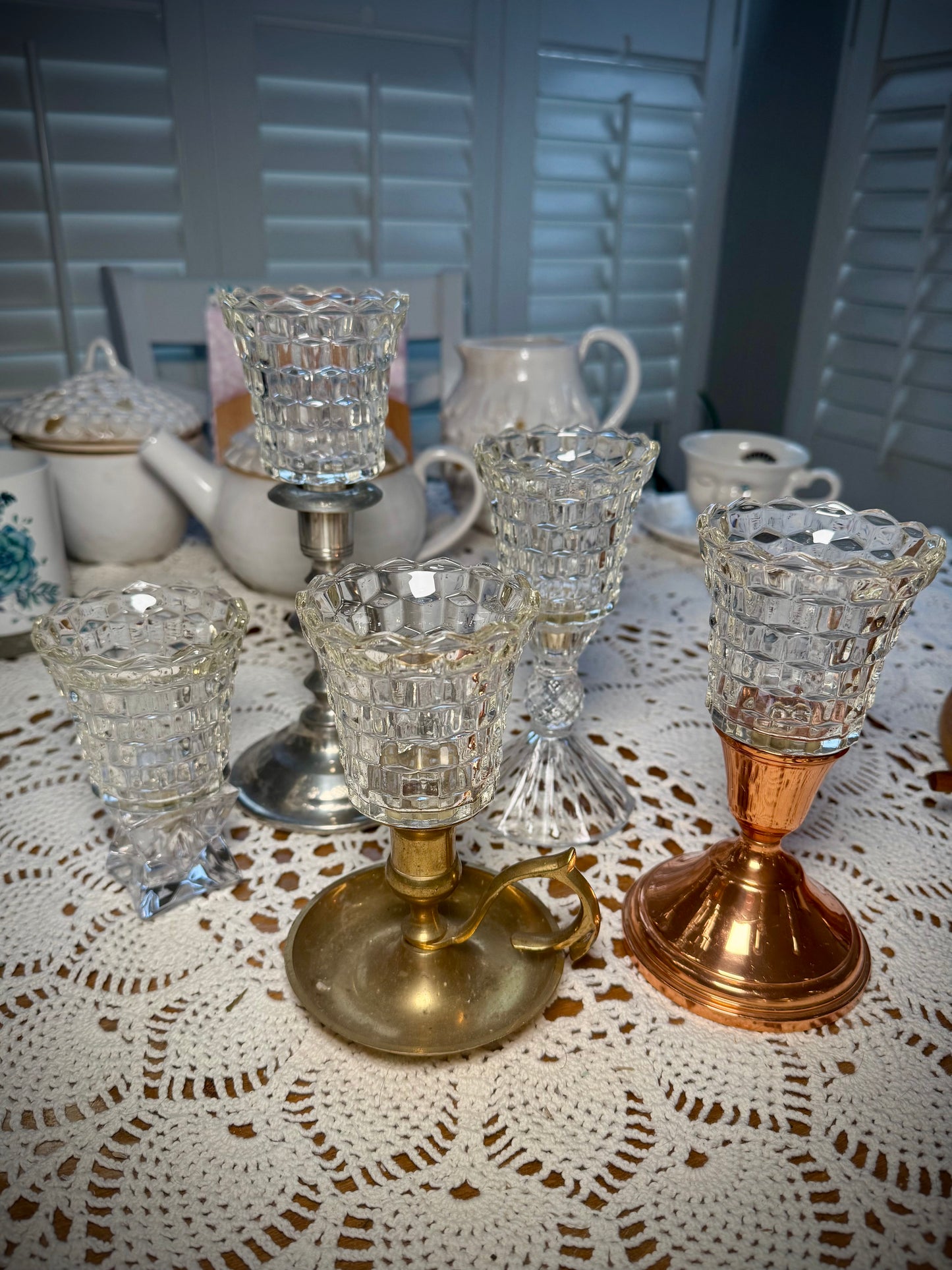 A collection of vintage glass votive holders with pegs and gaskets, displayed on a table with a lace tablecloth.