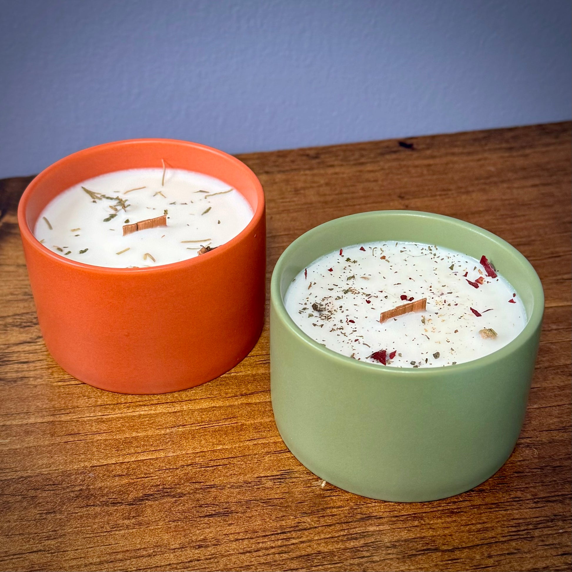 A burnt orange and a green ceramic candle sitting on a wooden surface.