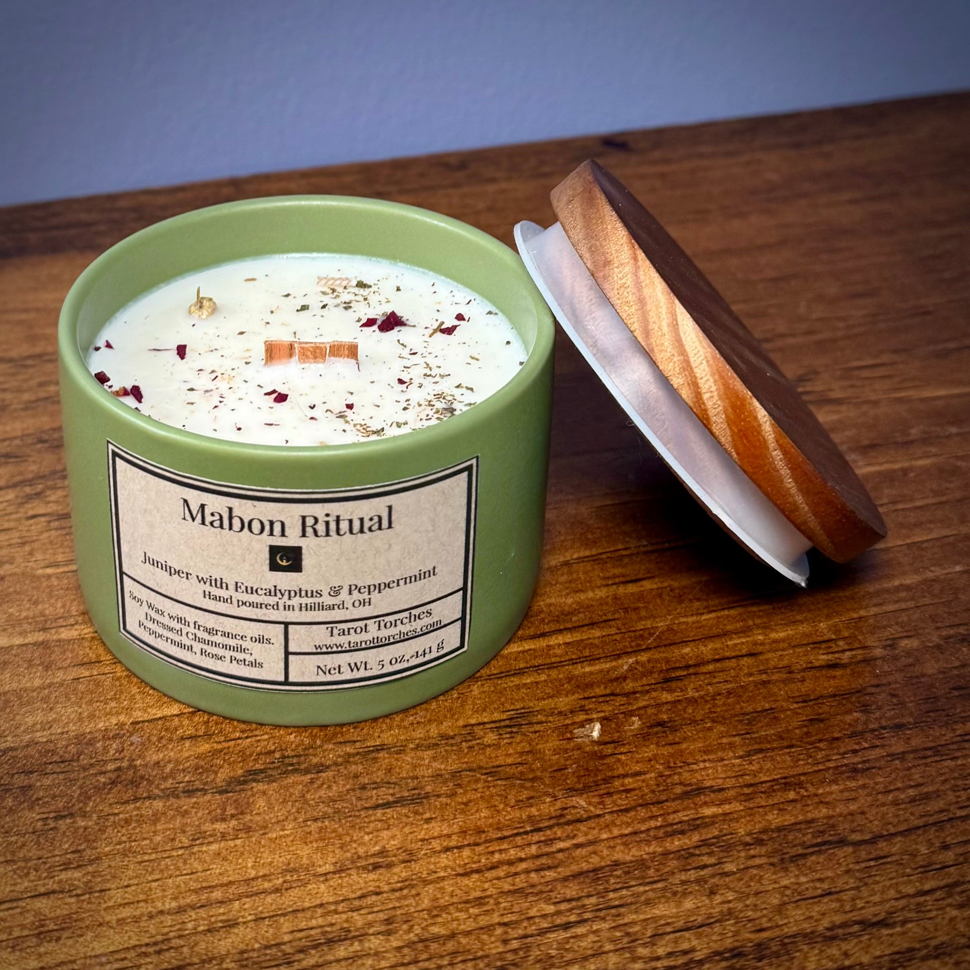 A greaan candle reading "Mabon Ritual" with an offset pine lid on a wooden surface.
