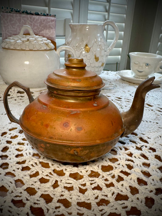 A vintage copper teapot with a Middle Eastern style design, placed on a table with a white lace tablecloth.
