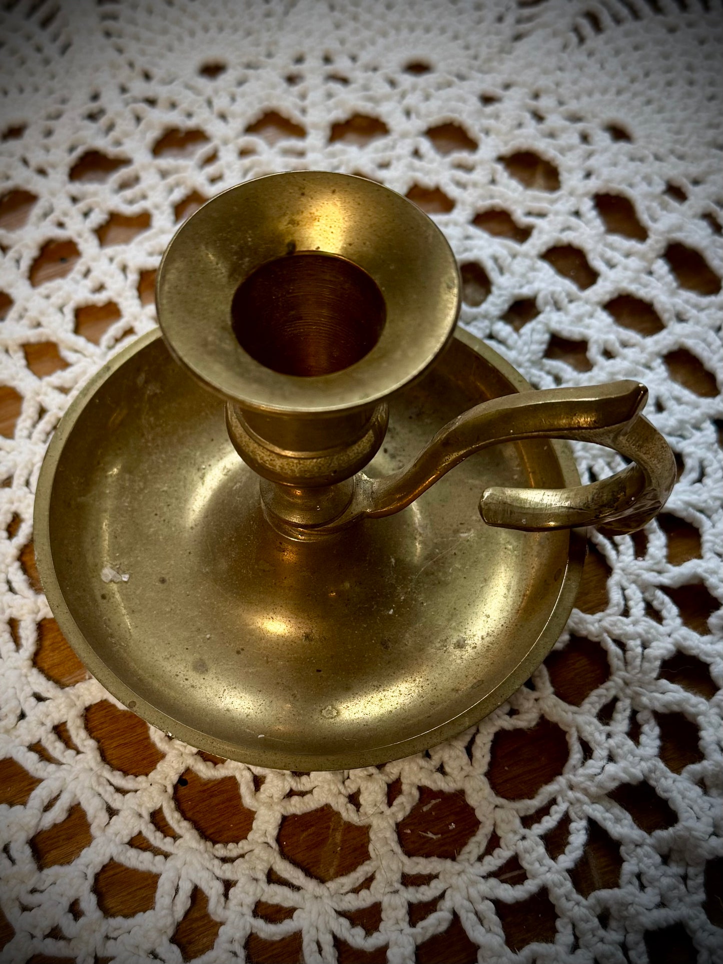 A vintage brass candlestick with a finger loop on a table with a lace tablecloth.
